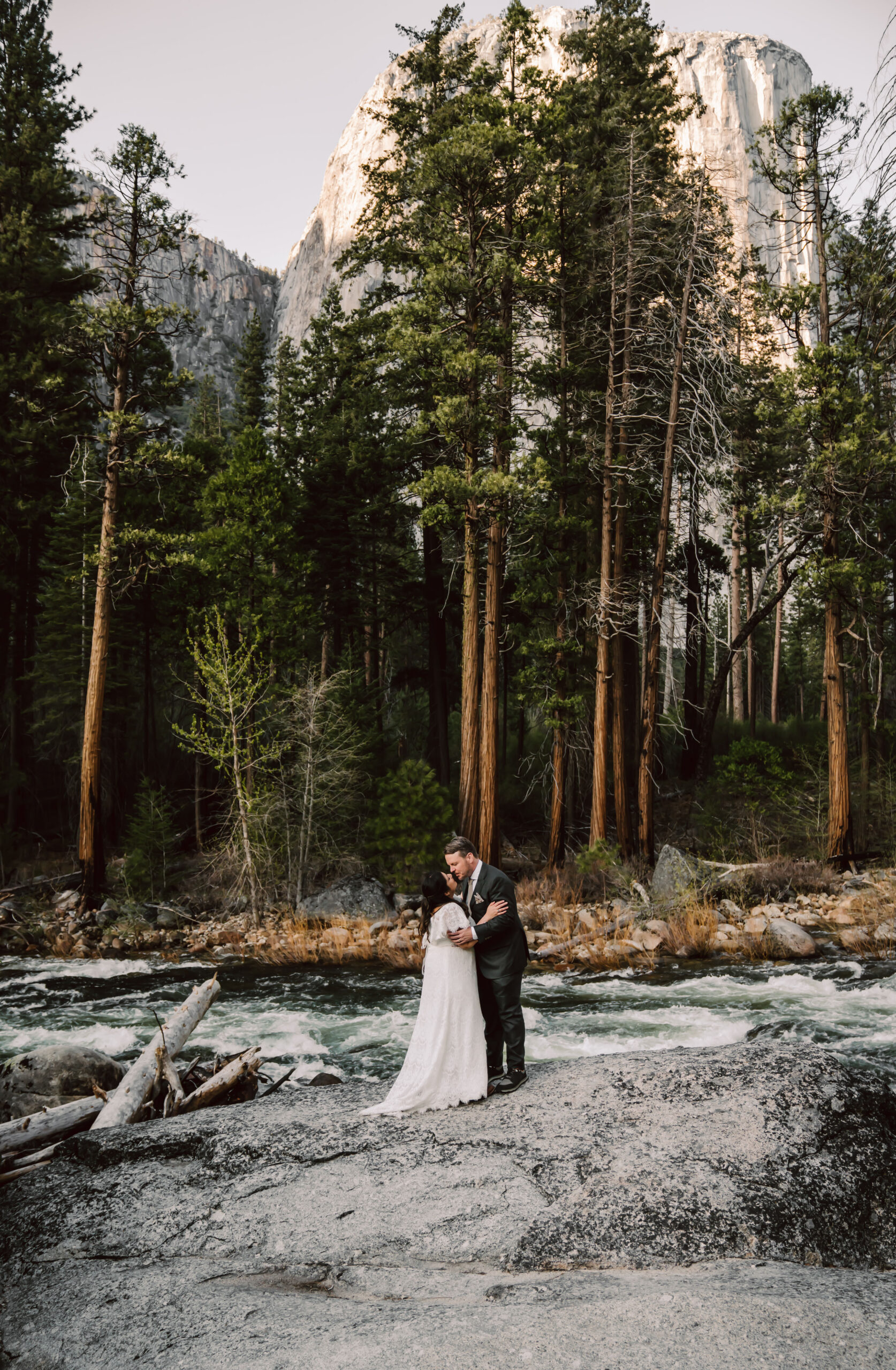 A elopement couple kissing next to the river and forest in the backdrop for their Yosemite Elopement
