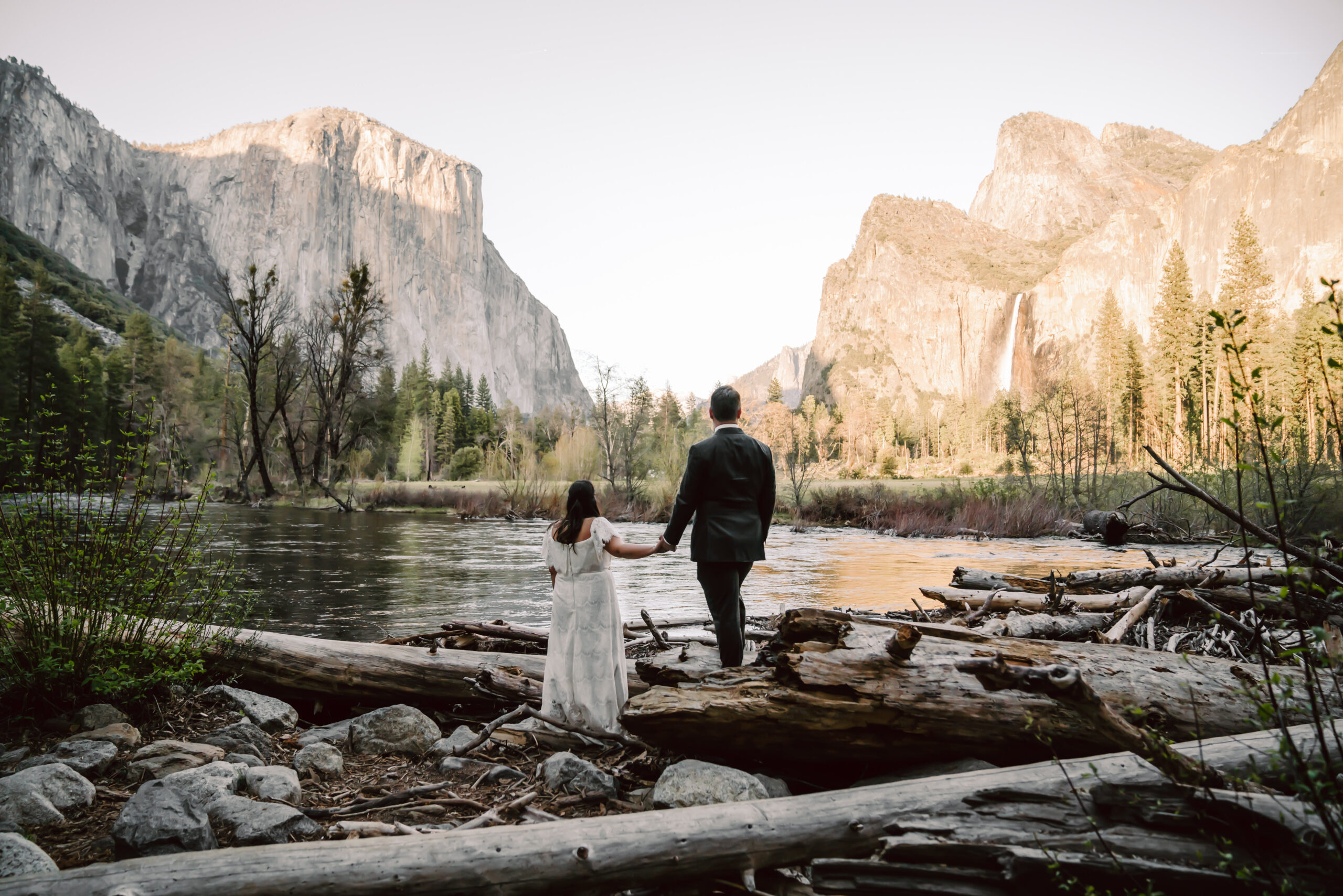 A recently married couple standing on a log overlooking Yosemite Valley View during sunset on their elopement day