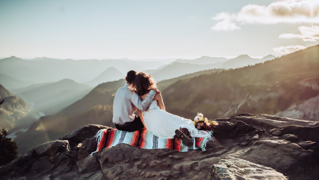A elopement couple sitting on a mountain blanket enjoying the sunrise
