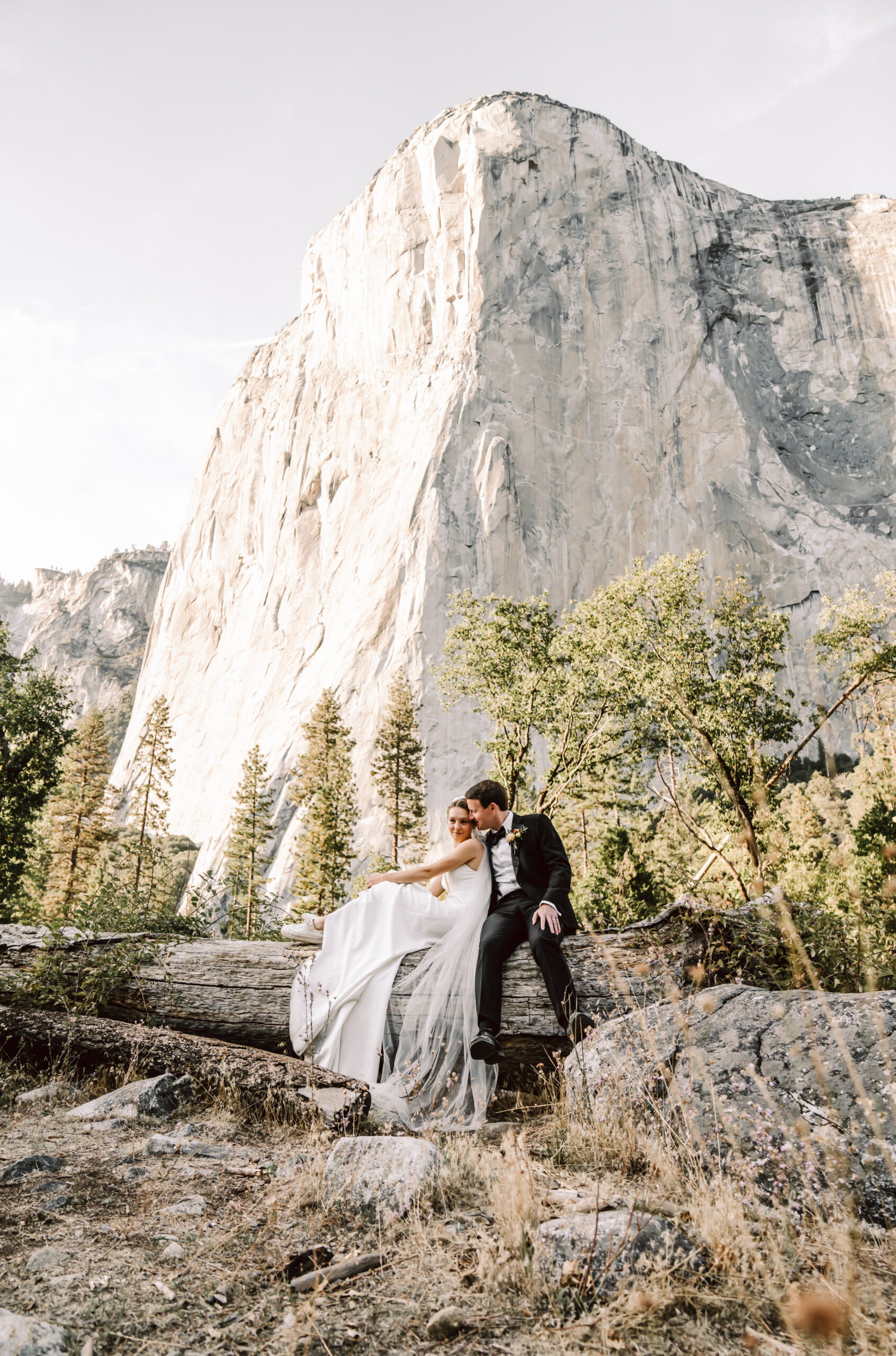 A wedding couple sitting on a log with El Cap in the background for their Yosemite Elopement 