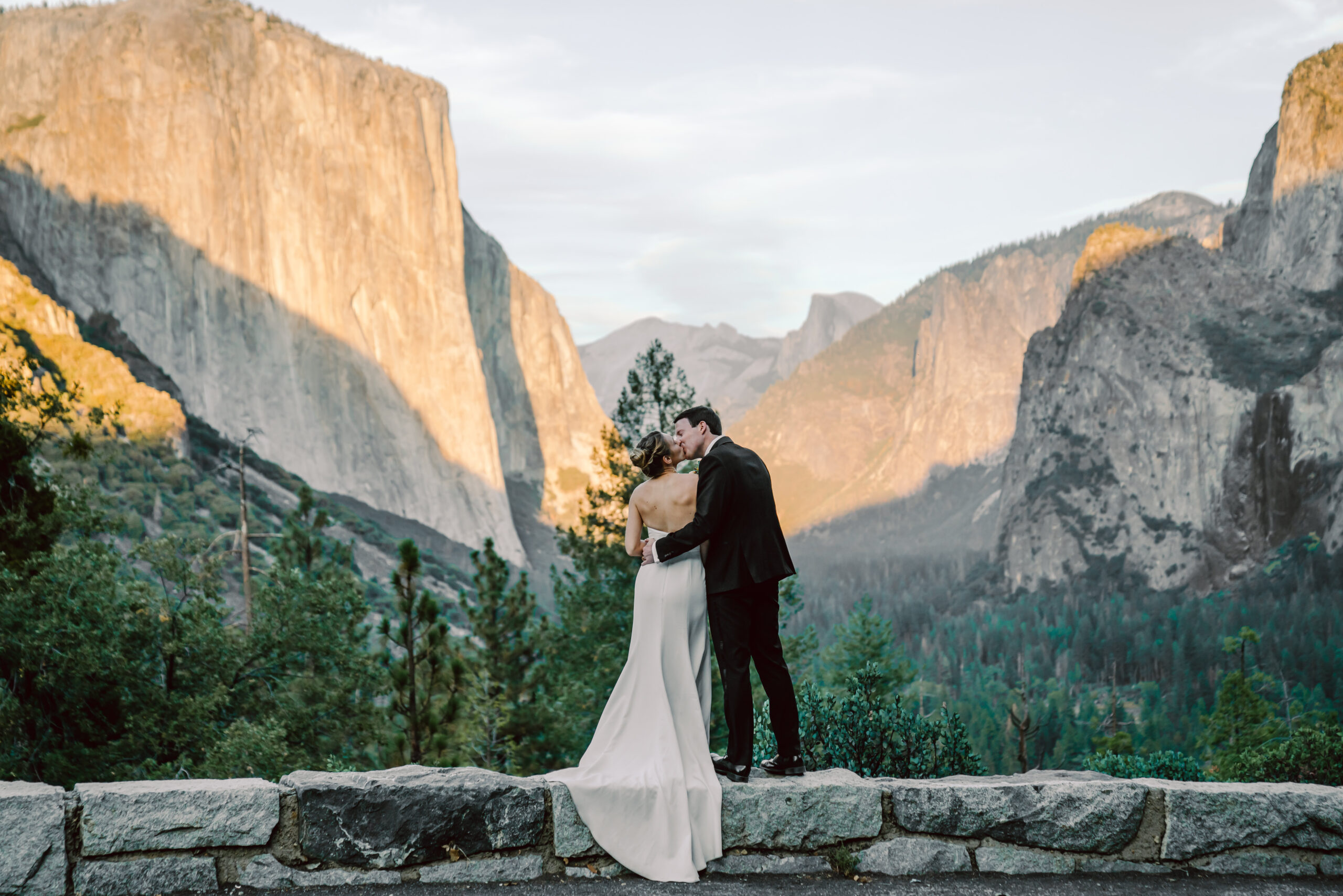 A wedding couple standing on the wall edge at Tunnel View overlooking Yosemite Valley for their elopement day