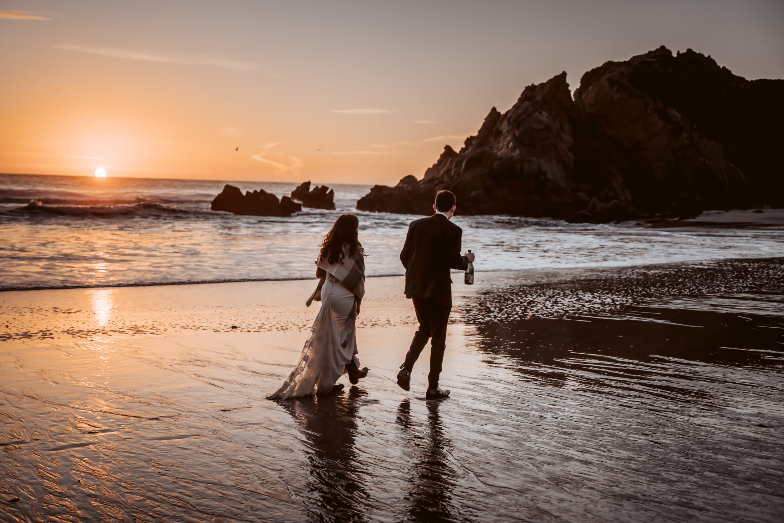 a bride and groom walking on the beach a sunset in Big Sur