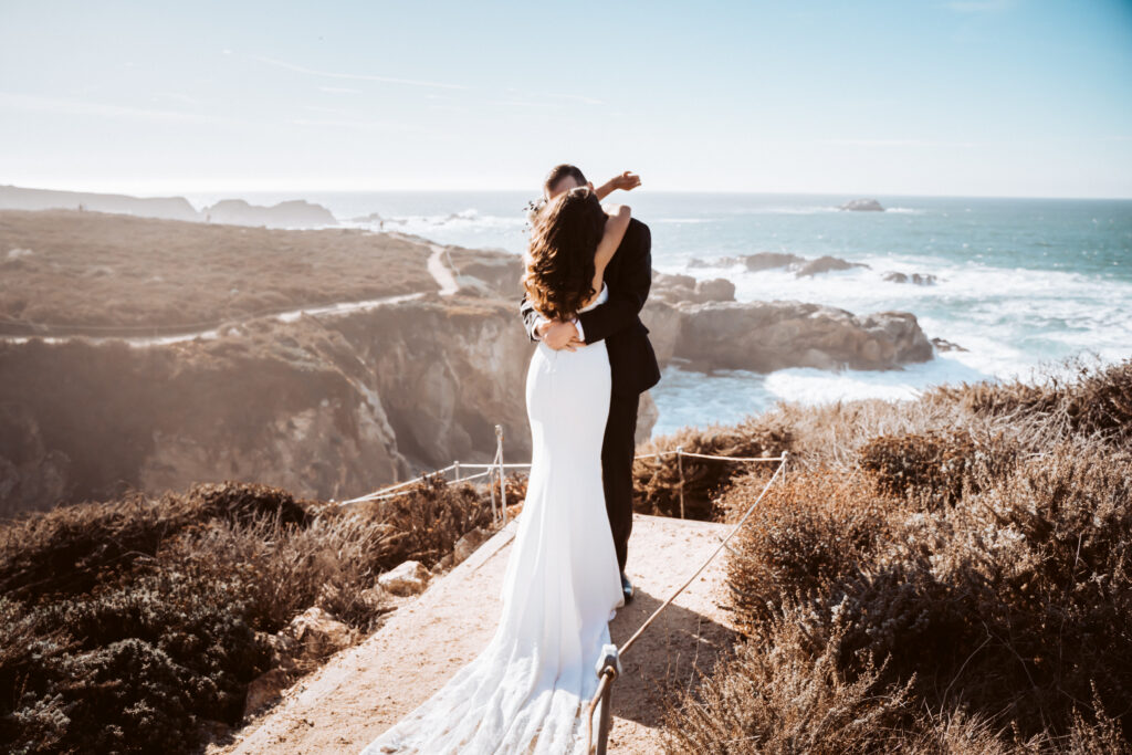 A bride and groom hugging overlooking the cliffs of Big Sur for their Elopement day