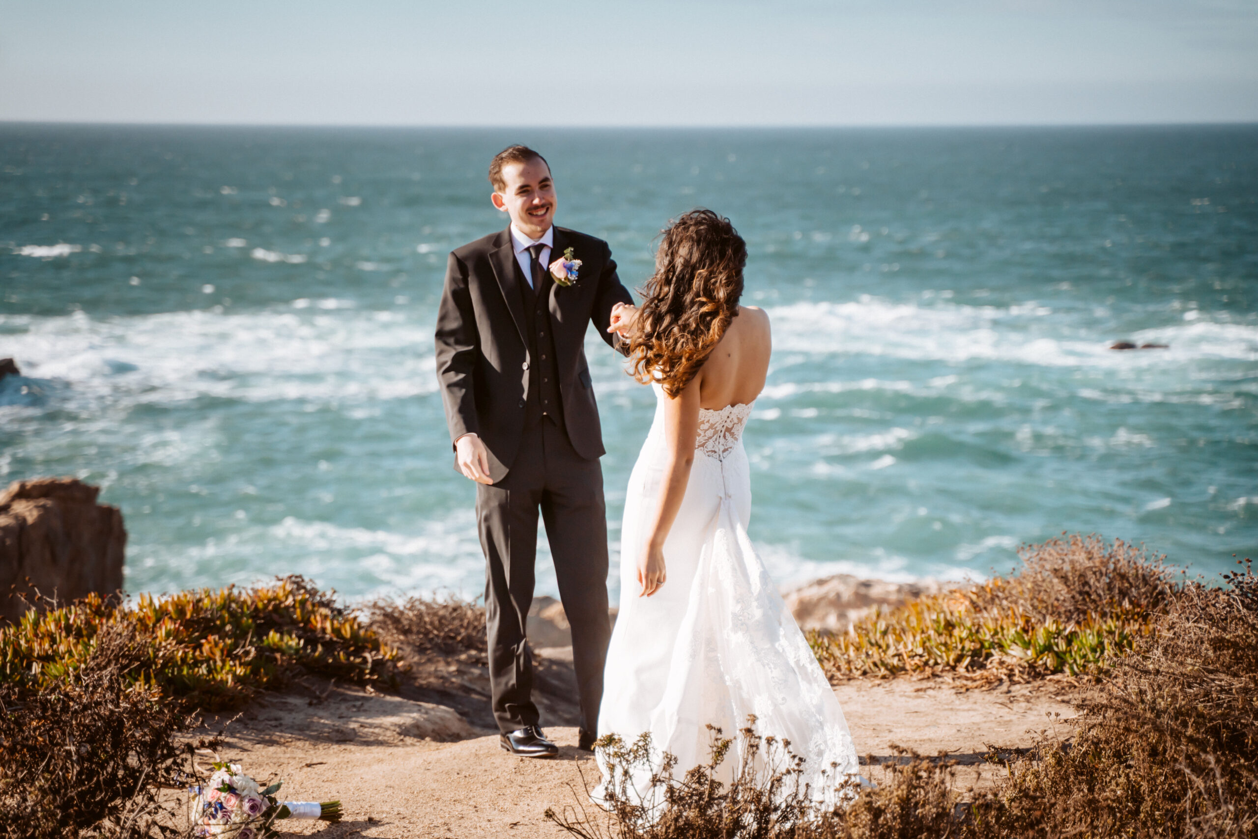 Bride and groom dancing on a cliff of Big Sur overlooking the blue ocean on their elopement day