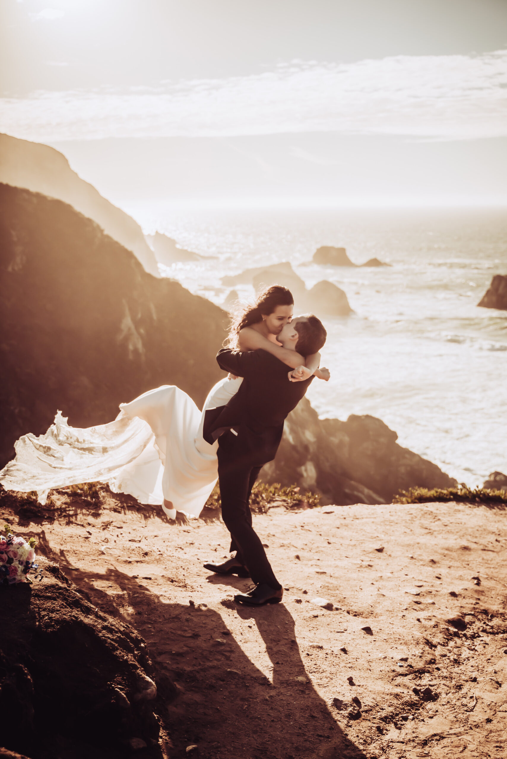 A groom holding up his bride on the cliffs of Big Sur for their elopement day 