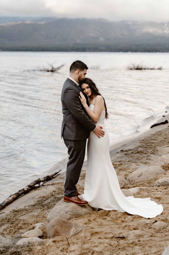 A groom holding his bride on the beach in Lake Tahoe for their Elopement day