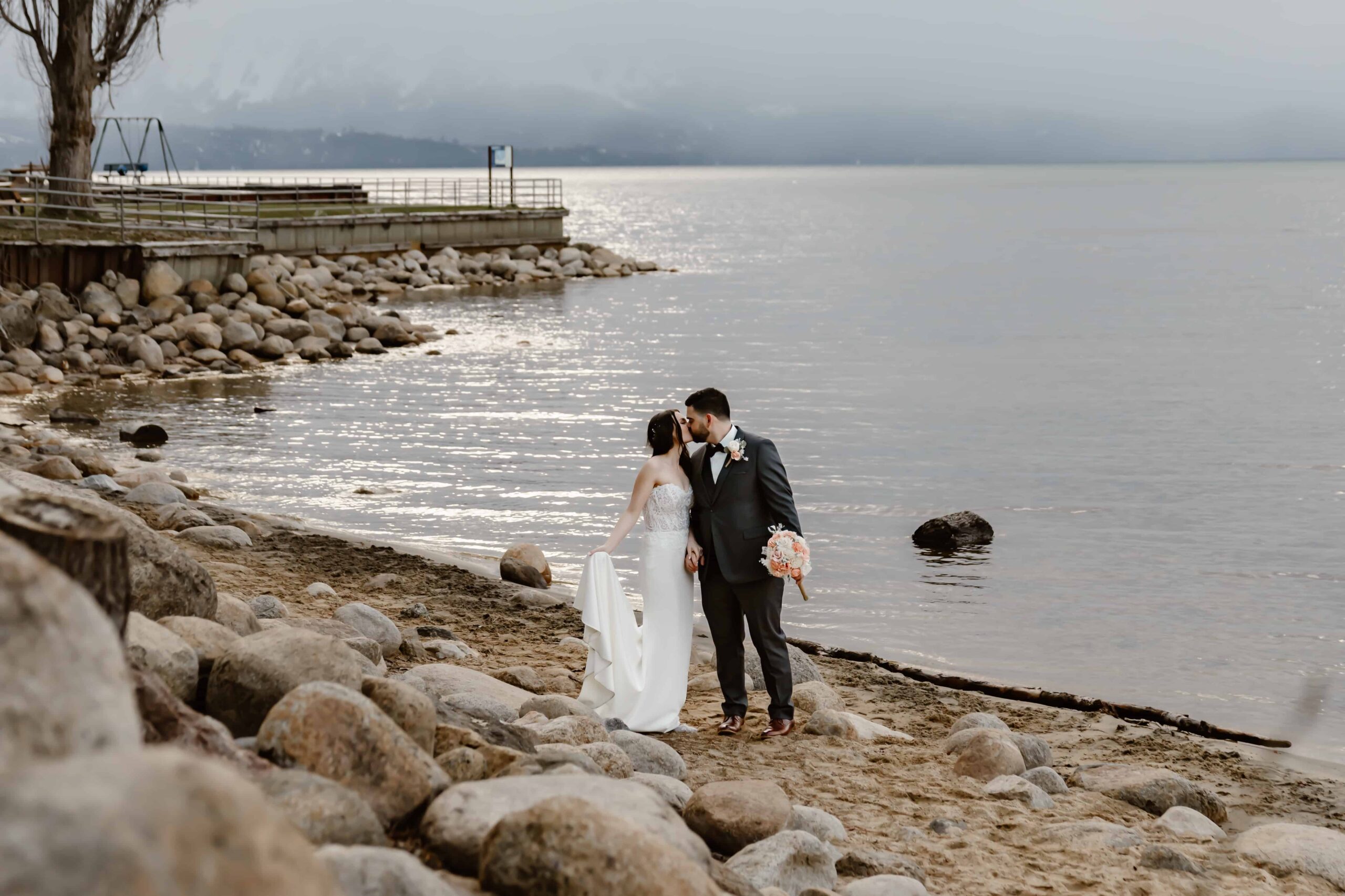 A bride and groom kissing on the beach by the water of Lake Tahoe for their wedding day