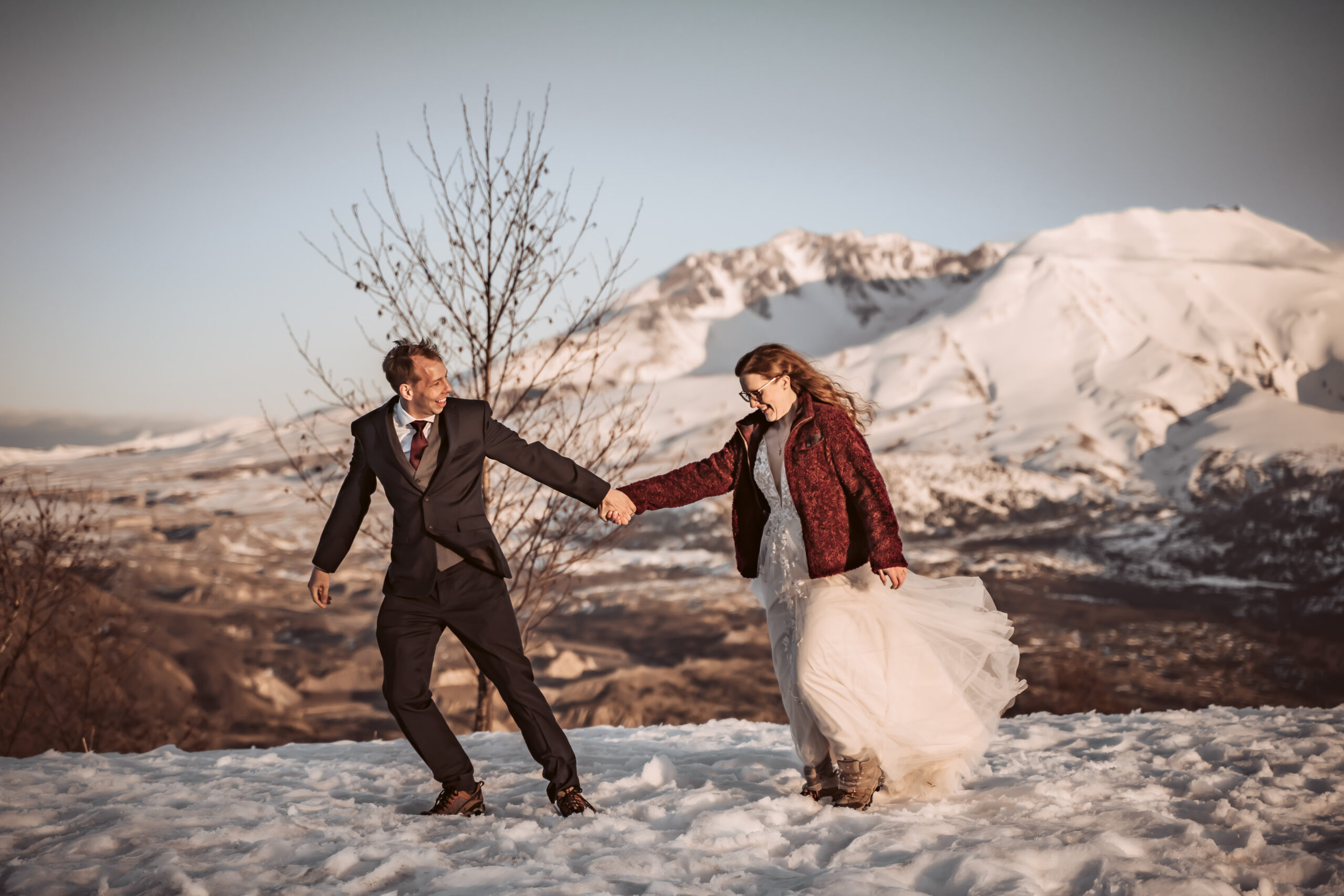a groom pulling his bride in the snow with Mount Saint Helens in the backdrop