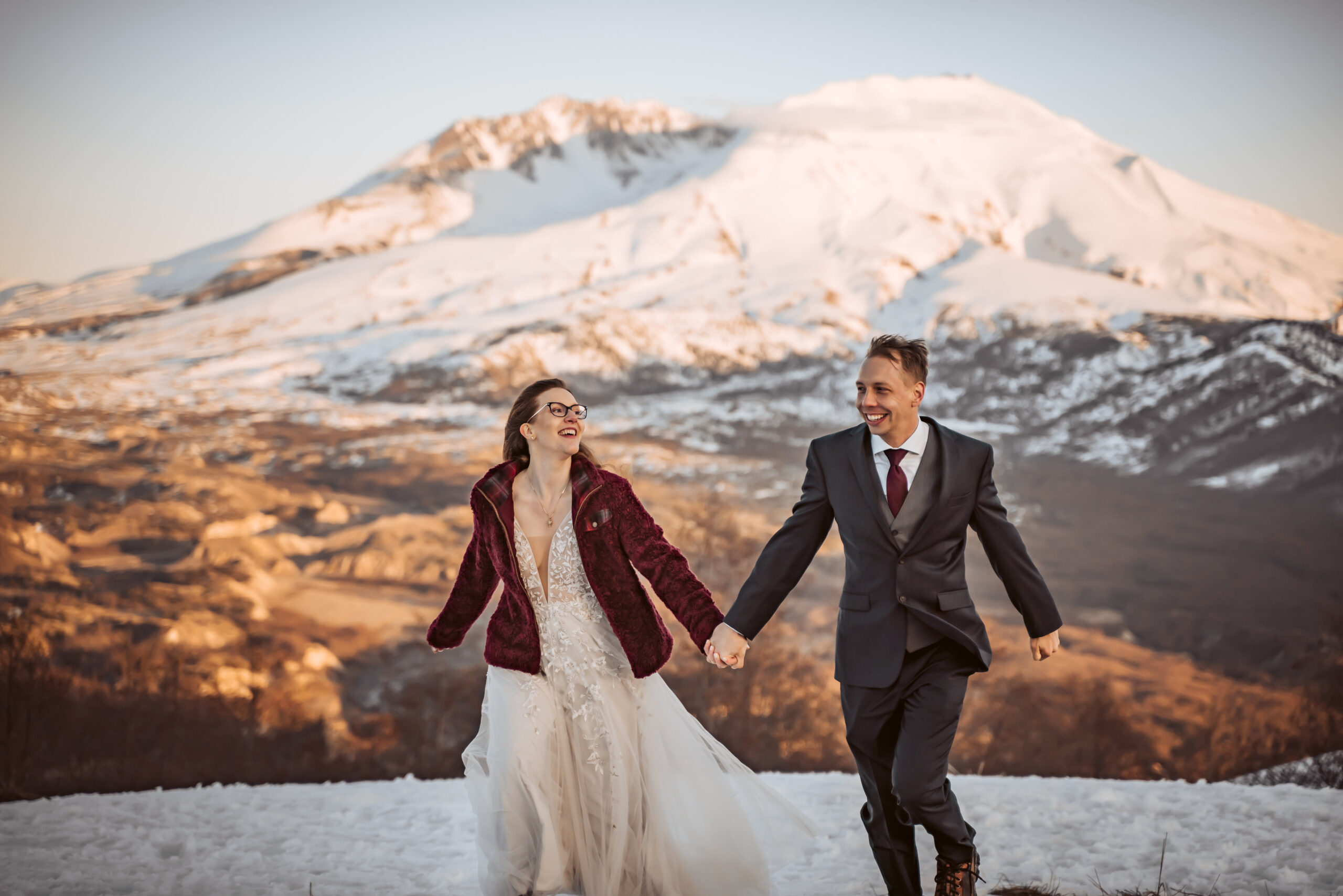  a recently married couple running in the snow with Mount Saint Helen's in the background