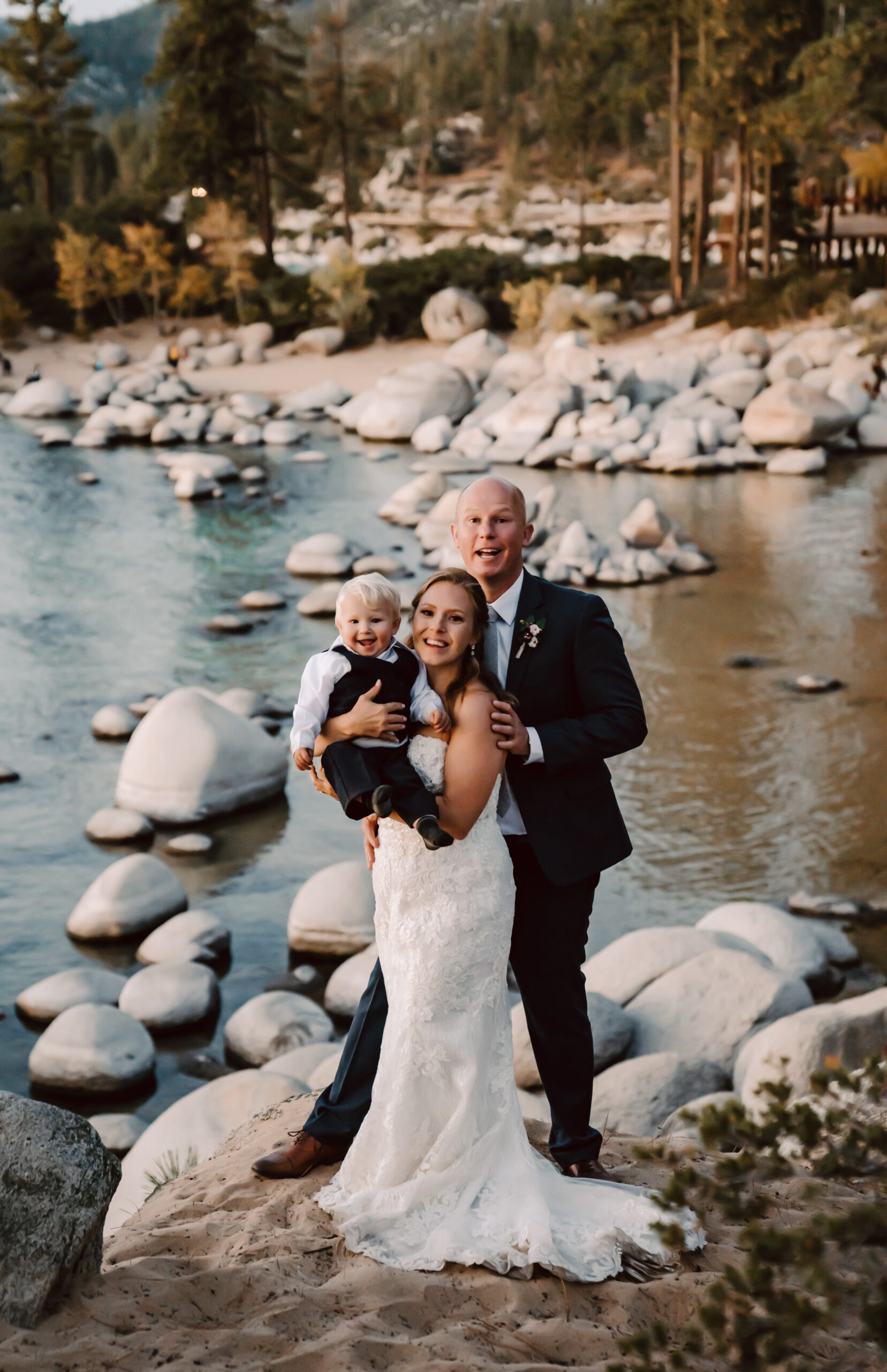 A bride and a groom holding their little one on their elopement day in front of Sand Harbor for their Lake Tahoe elopement