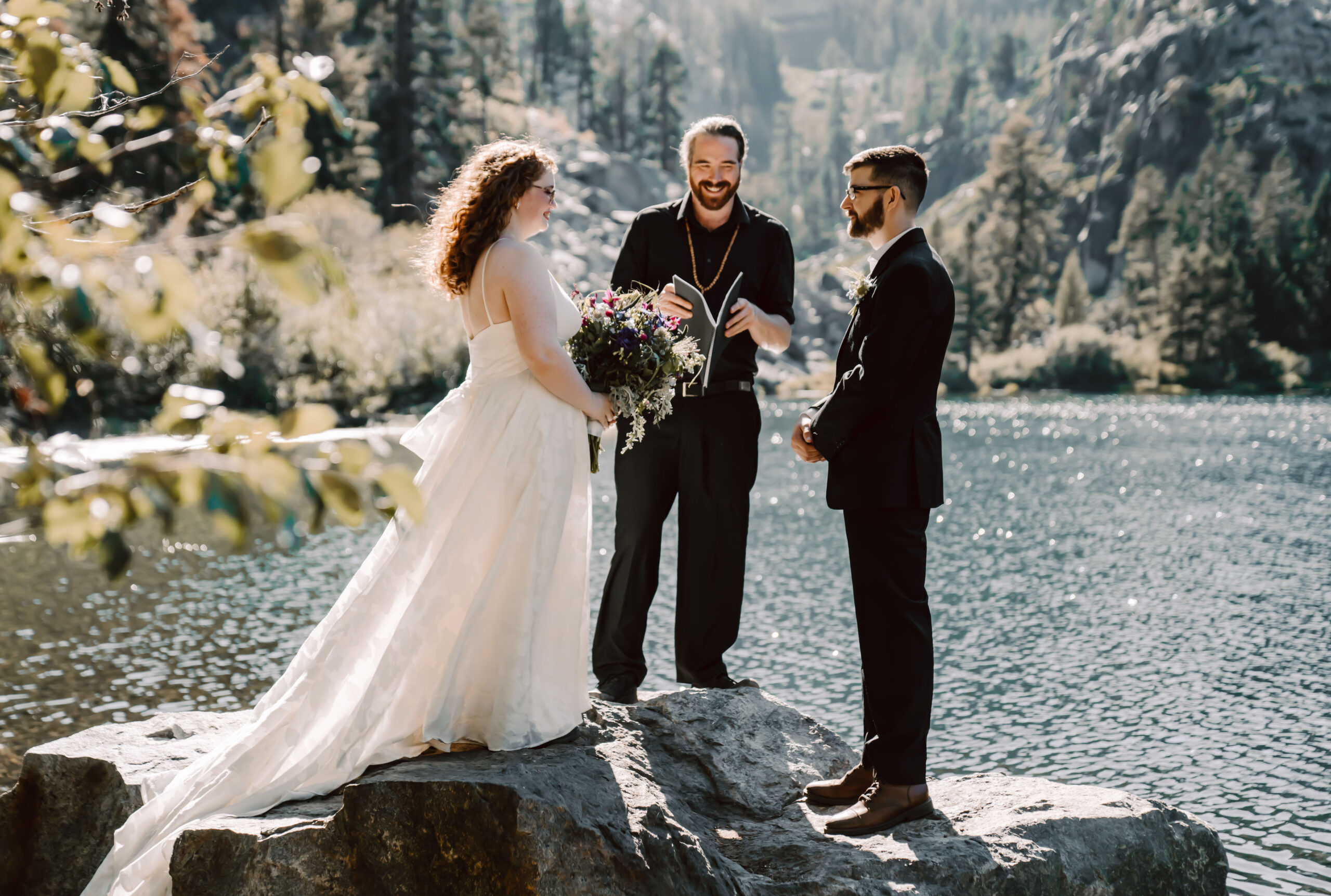 A bride and groom standing on a rock overlooking a lake for their elopement ceremony in California