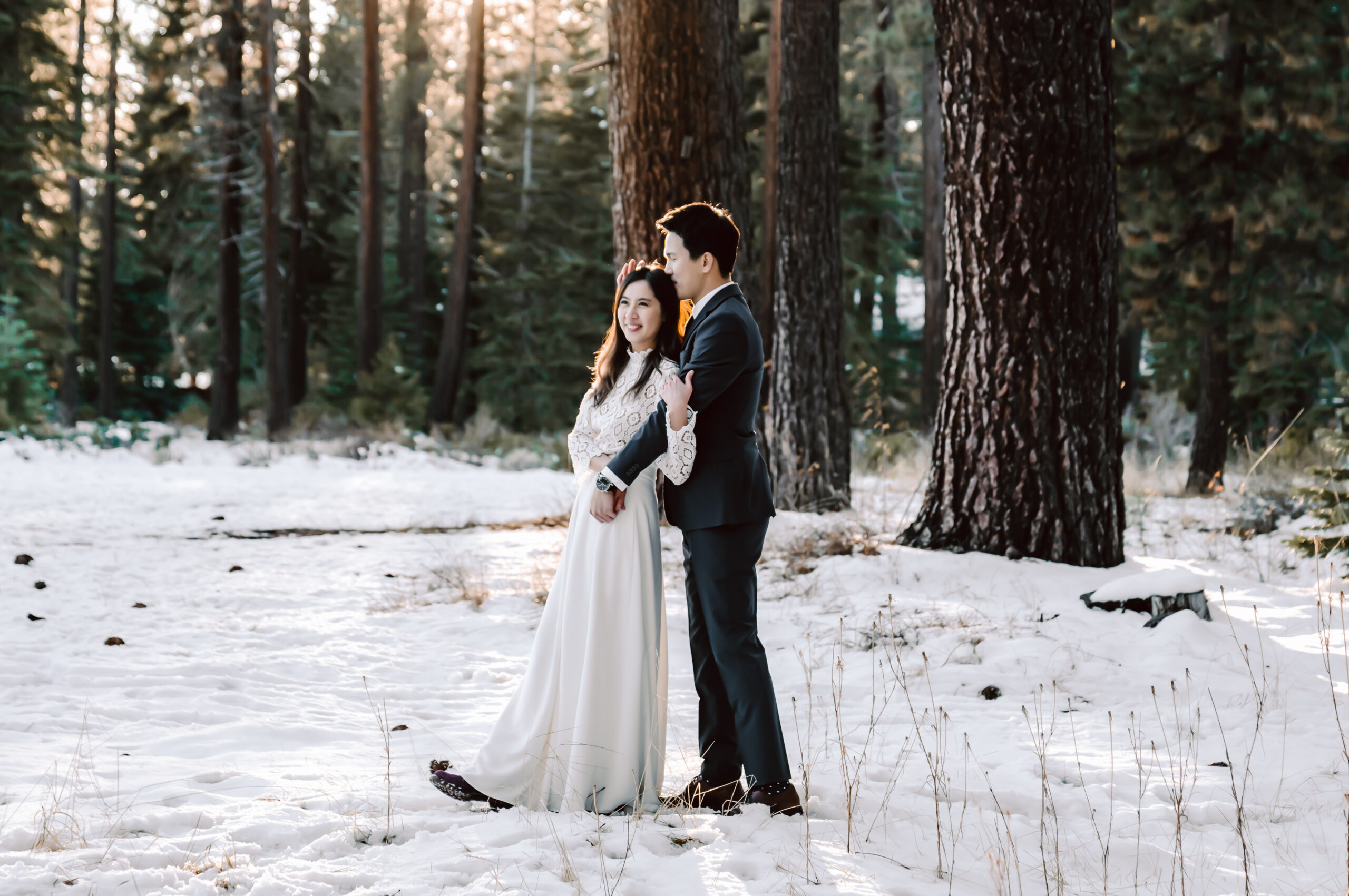 A bride and groom hugging and standing in the snow with the forest in the background for their elopement day in California