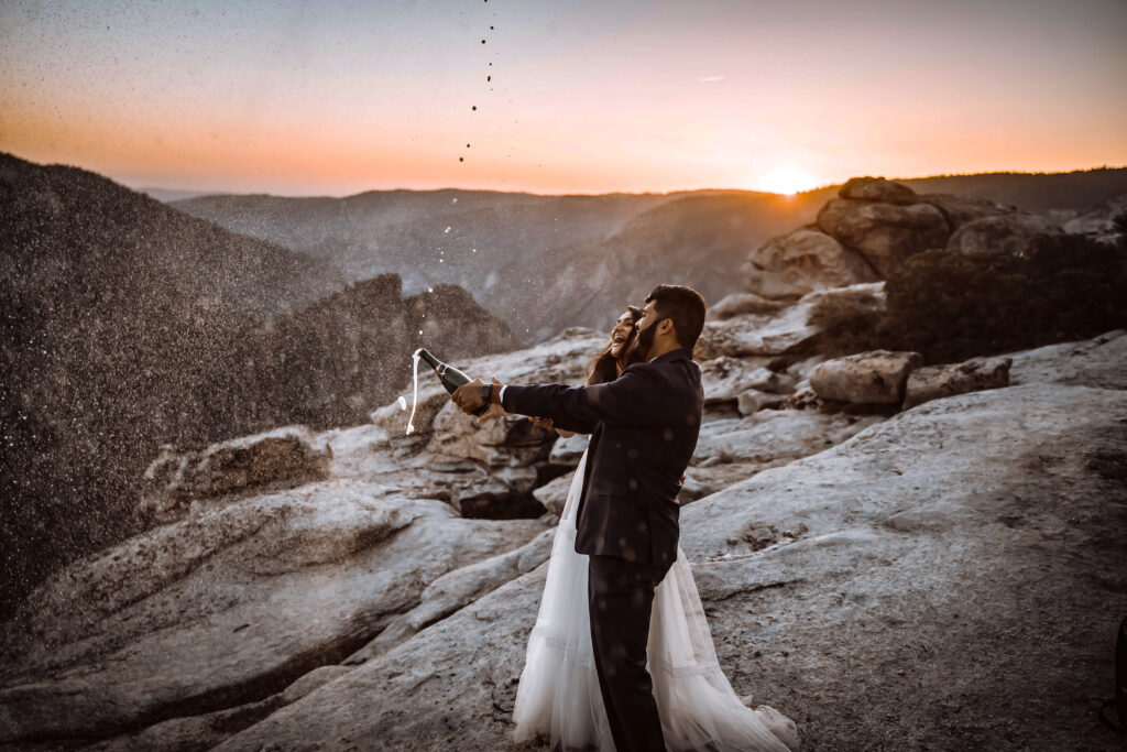 A bride and groom spraying champagne all over during sunset at Taft Point in Yosemite valley for their elopement day 