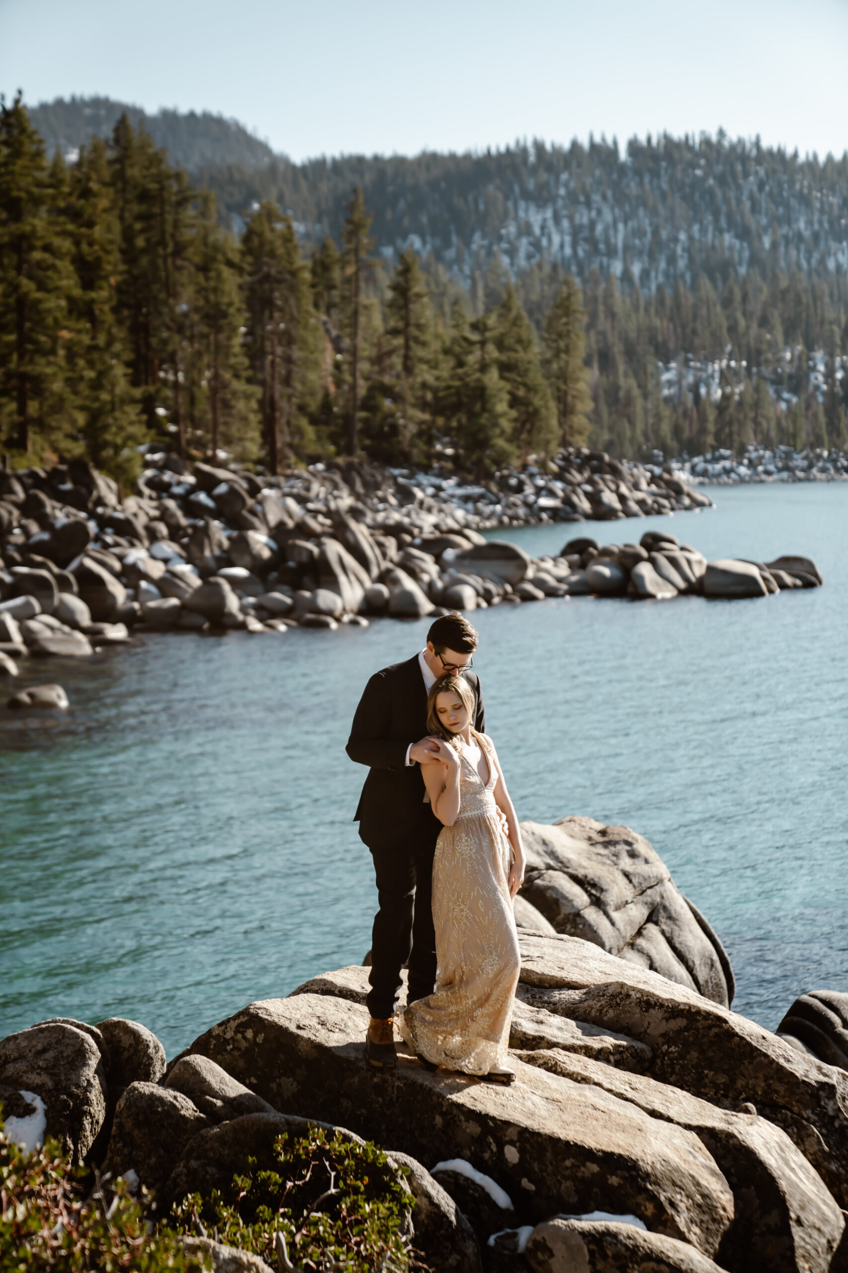 A bride and groom standing on a big boulder overlooking secret Cove in Lake Tahoe for their elopement day