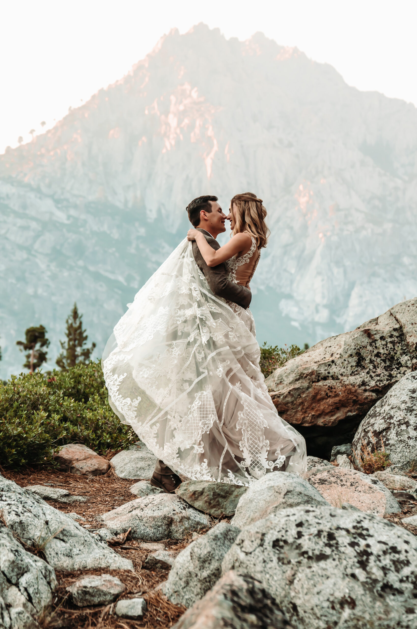 A bride wrapping her dress around her groom in front of a hazy mountain for their Lake Tahoe Elopement