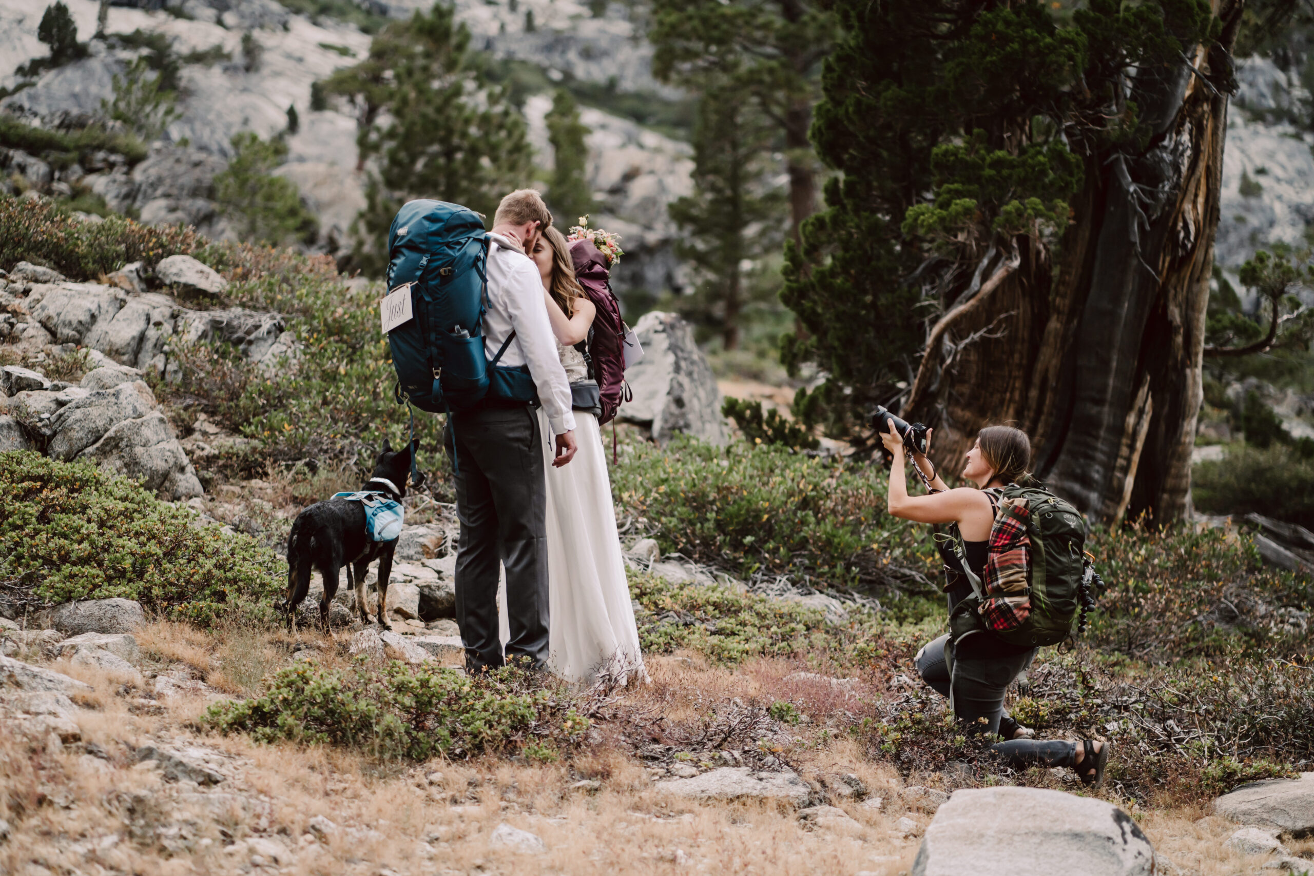 An elopement photographer taking pictures of a elopement couple kissing and wearing hiking backpacks for their adventure elopement