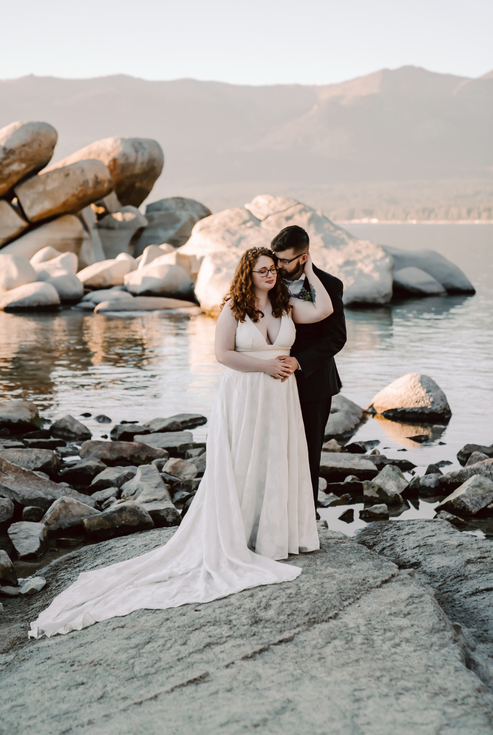 A bride and groom standing on a big boulder on the beach for their outdoor nature elopement
