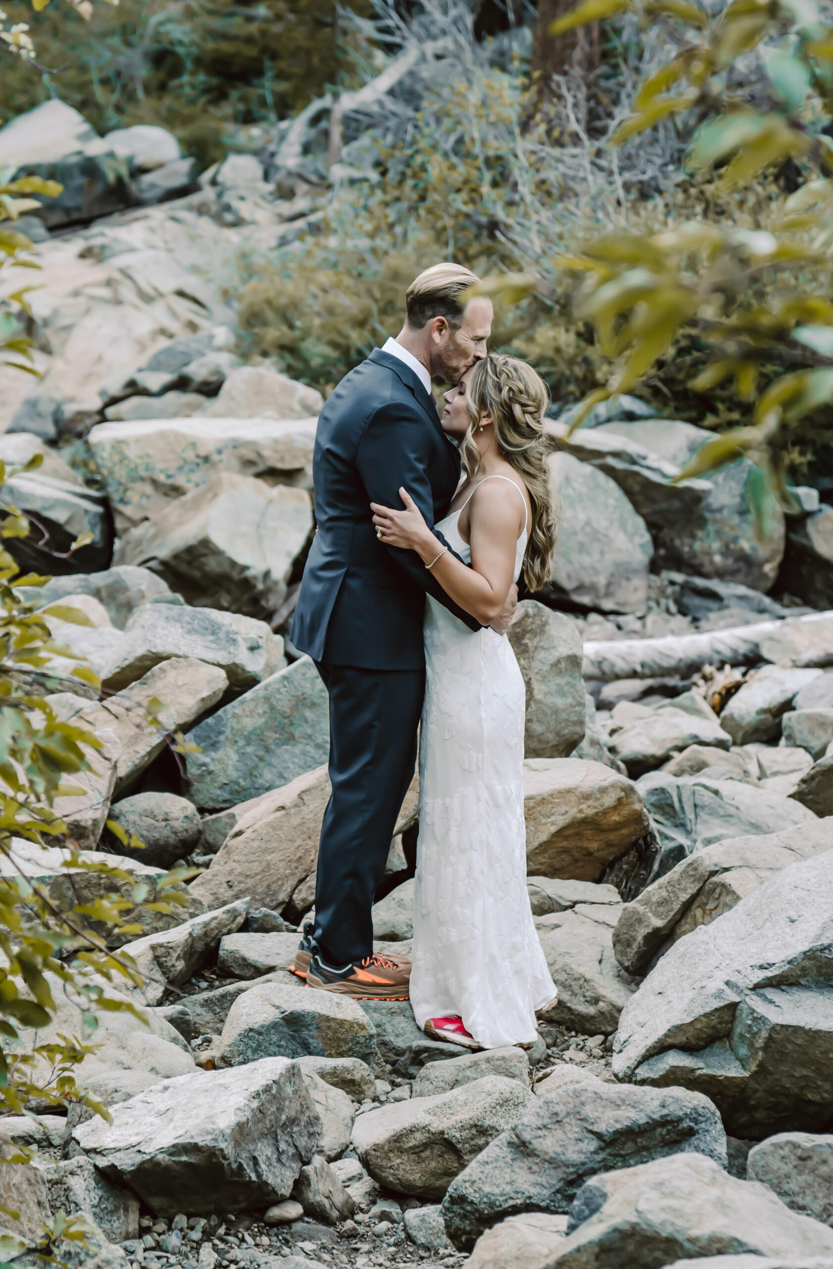 A groom kissing his bride and standing on the rocks in the forest for their nature elopement