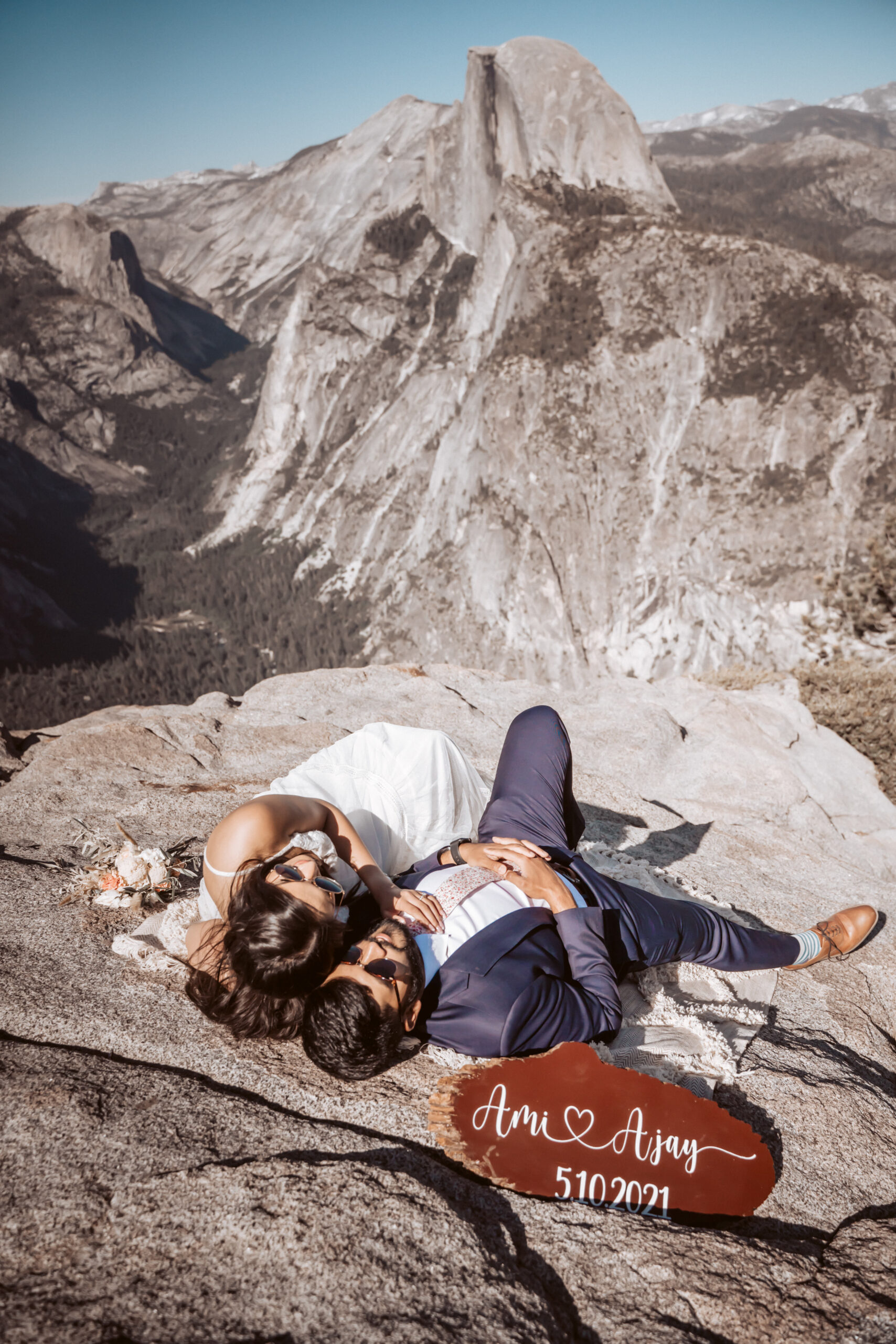 An elopement couple laying on the ground looking out onto half dome and yosemite valley for their glacier point Elopement