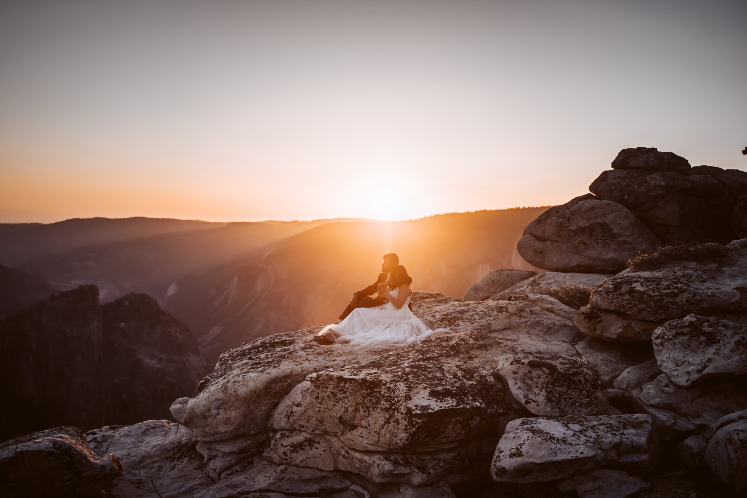 A wedding couple sitting on the ledge during sunset at their Taft Point Yosemite Elopement