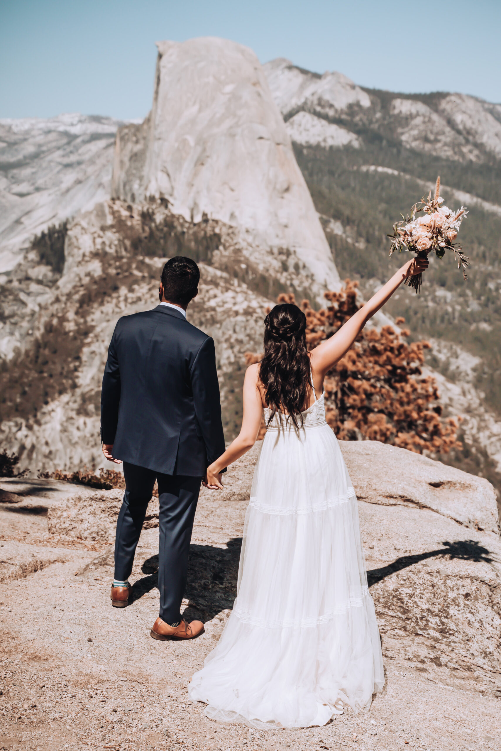 A wedding couple raising their hands in the air overlooking half dome for their Glacier Point Elopement in Yosemite