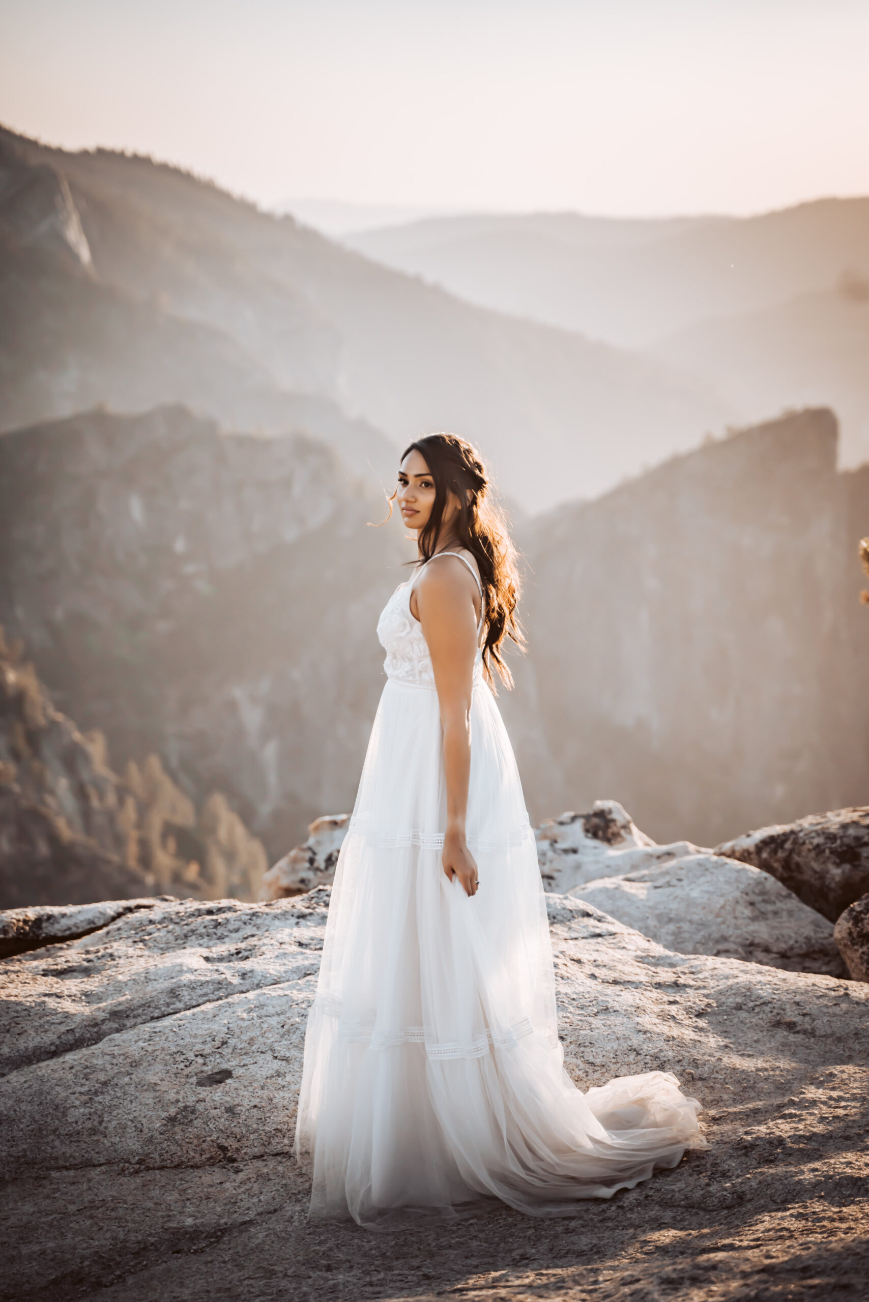 A bride standing on a cliff overlooking the sunset for her elopement in the Mountains