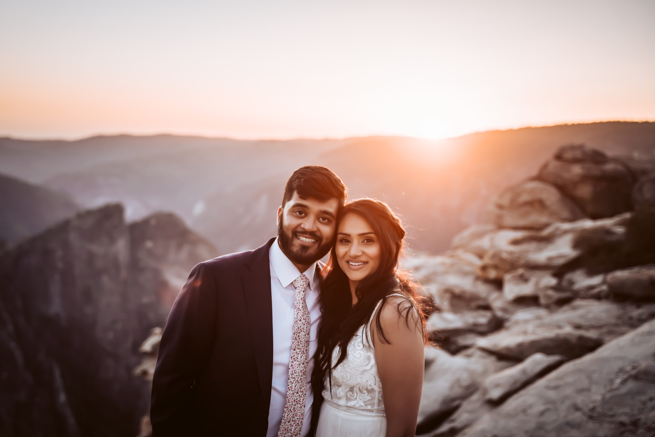 the bride and groom looking at the cameral with the sunset in the backdrop overlooking Yosemite Valley and the mountains
