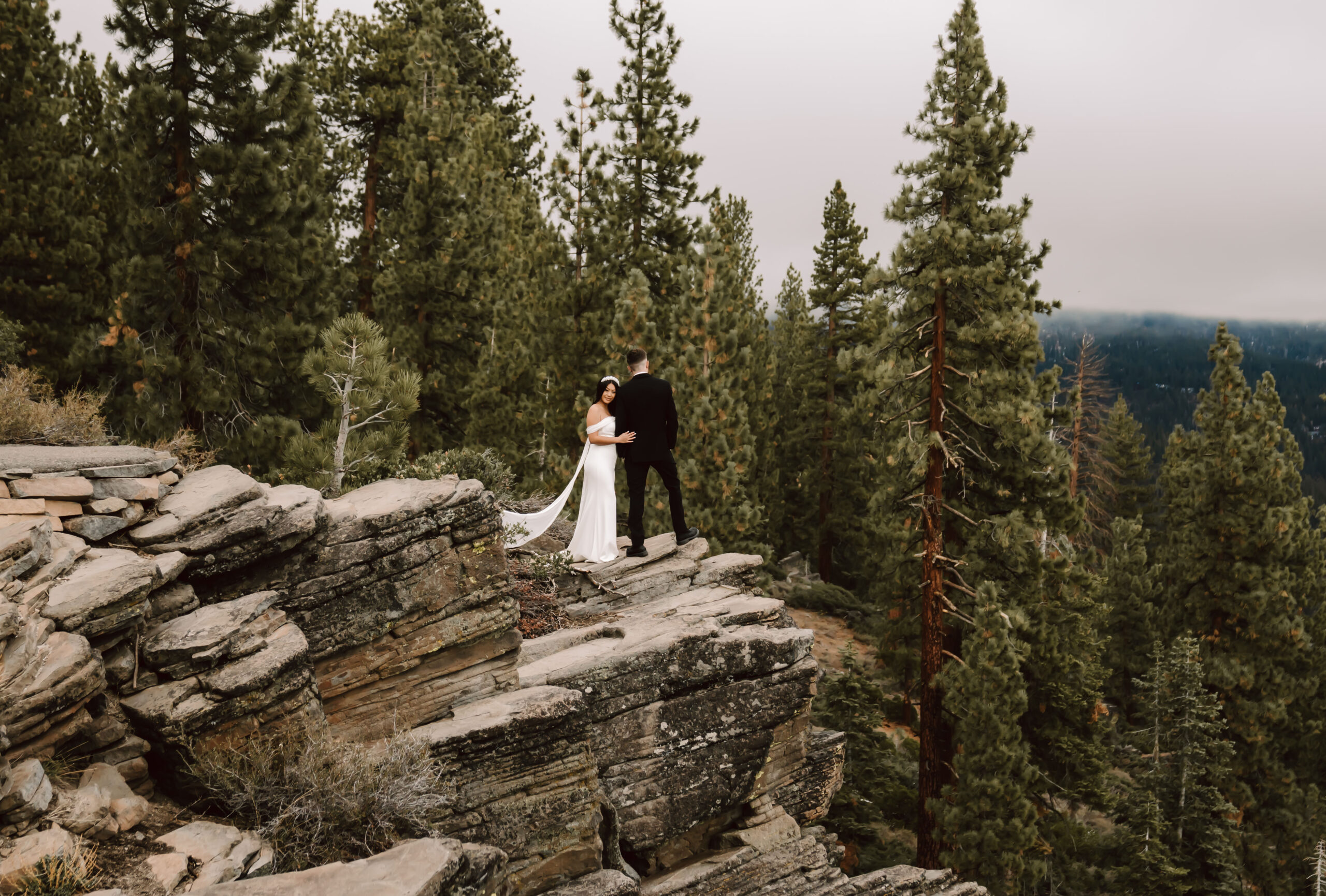 A bride and groom standing at the cliff overlooking the mountains on their Elopement day