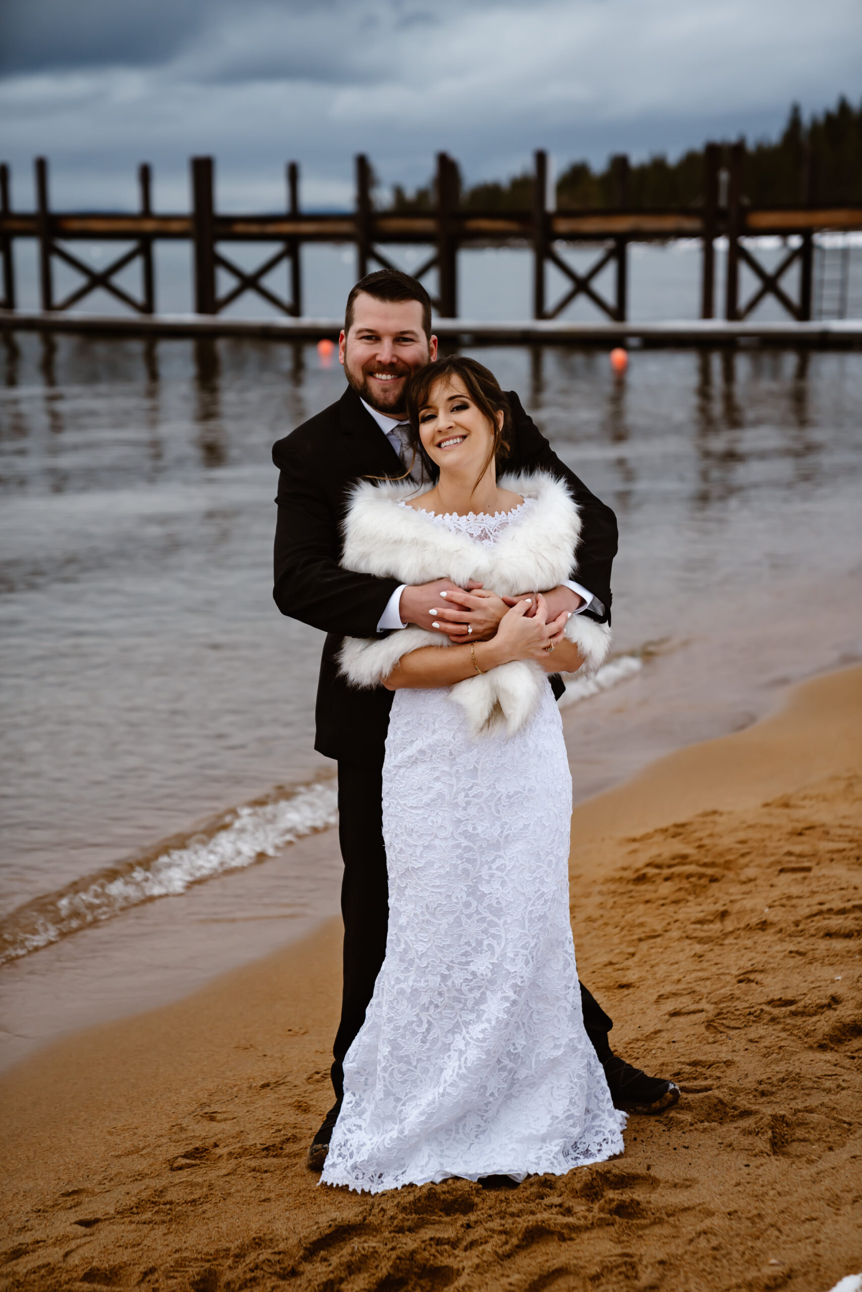 A bride and groom standing on the beach next to a pier for their elopement day