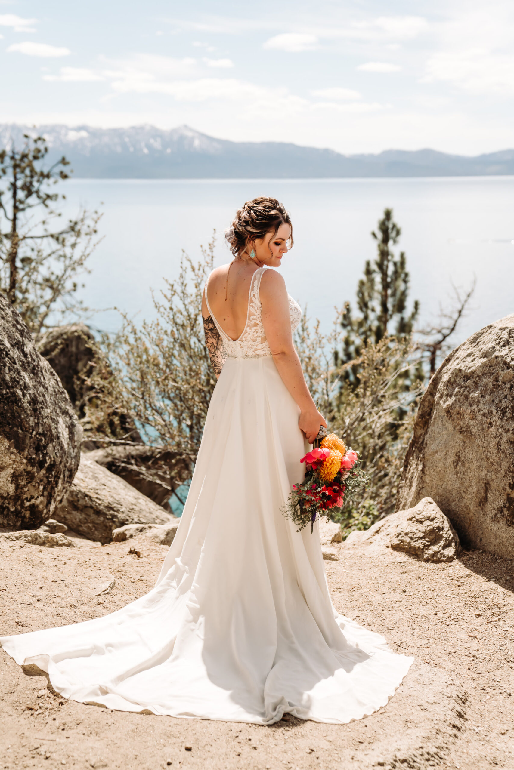 A bride showing the back of her elopement dress overlooking Lake Thaoe