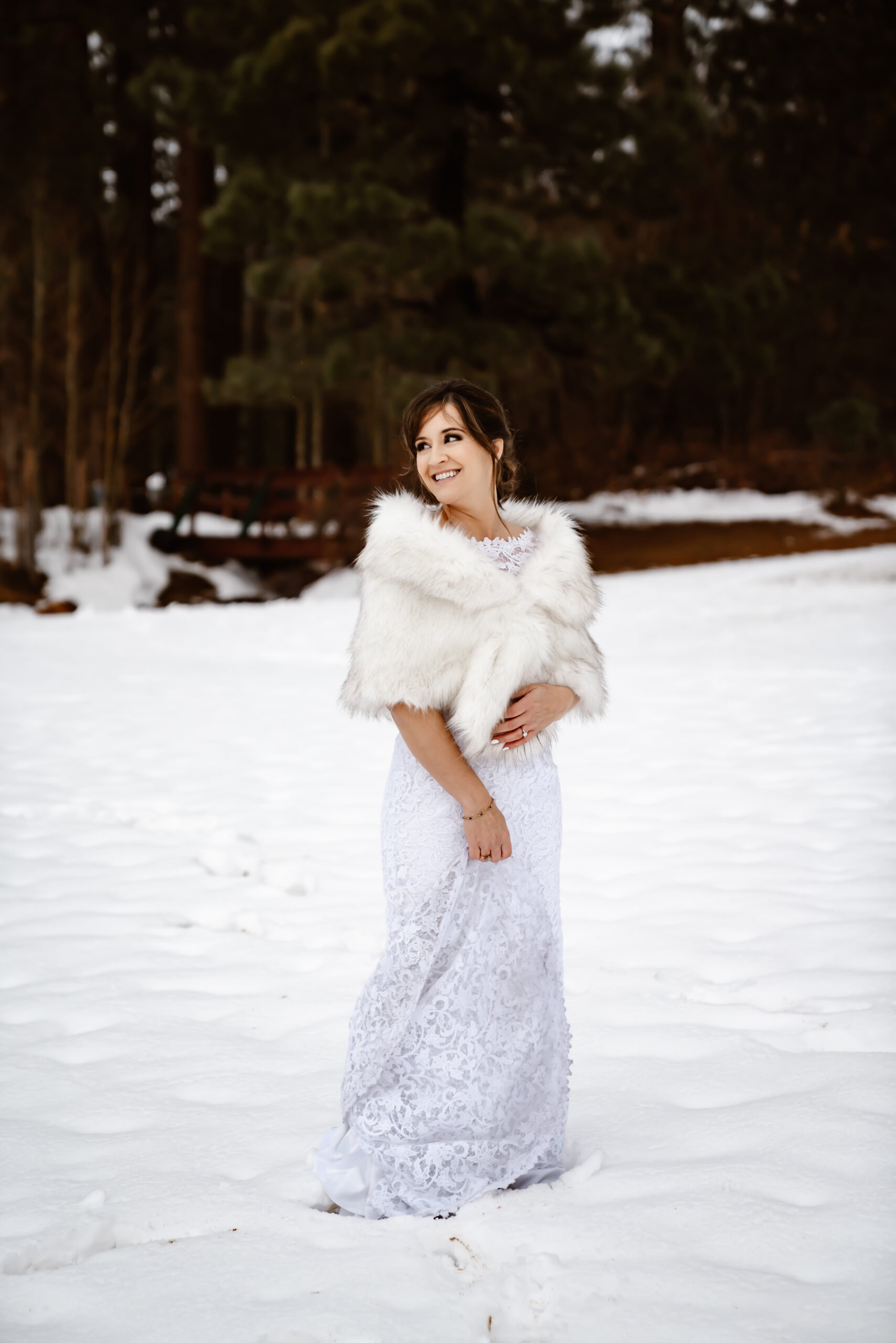 A bride wearing a lace elopement dress with a fur shawl dancing in the snow