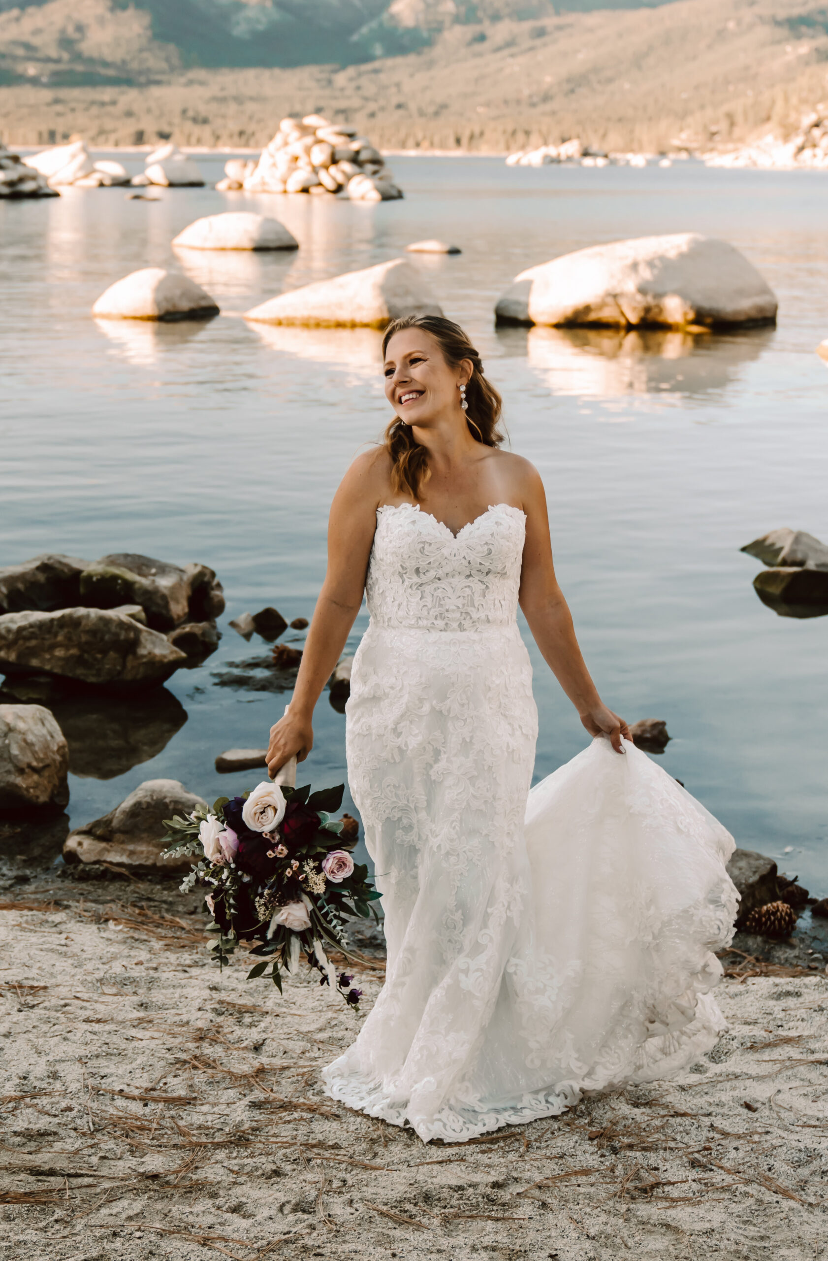 A bride dancing on the beach in a lace elopement dress next to Lake Tahoe
