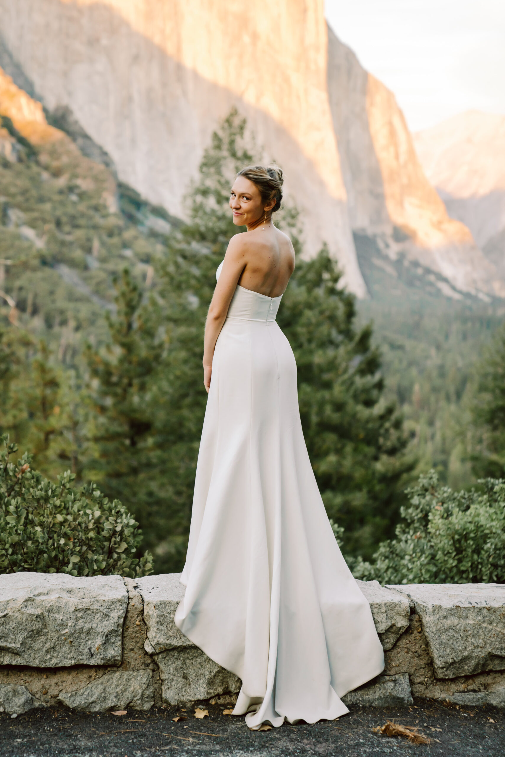 A bride standing in front of Yosemite Valley in a beautiful white dress with a long train for her elopement day
