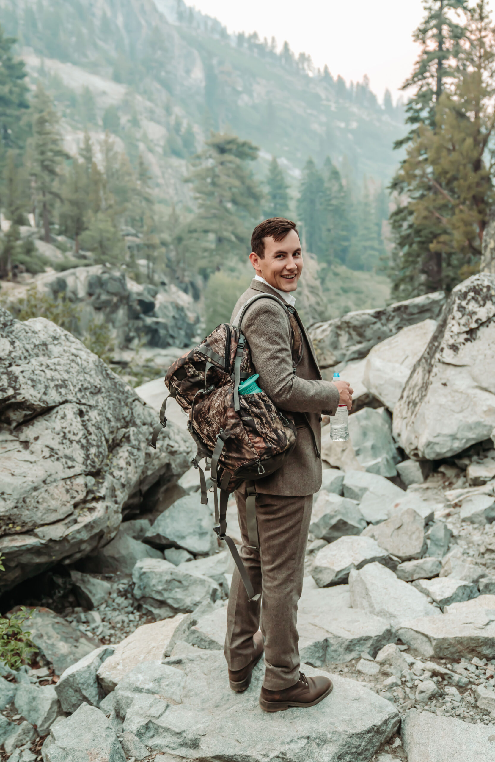 a groom in a grey tweed suit and backpack for his hiking elopement