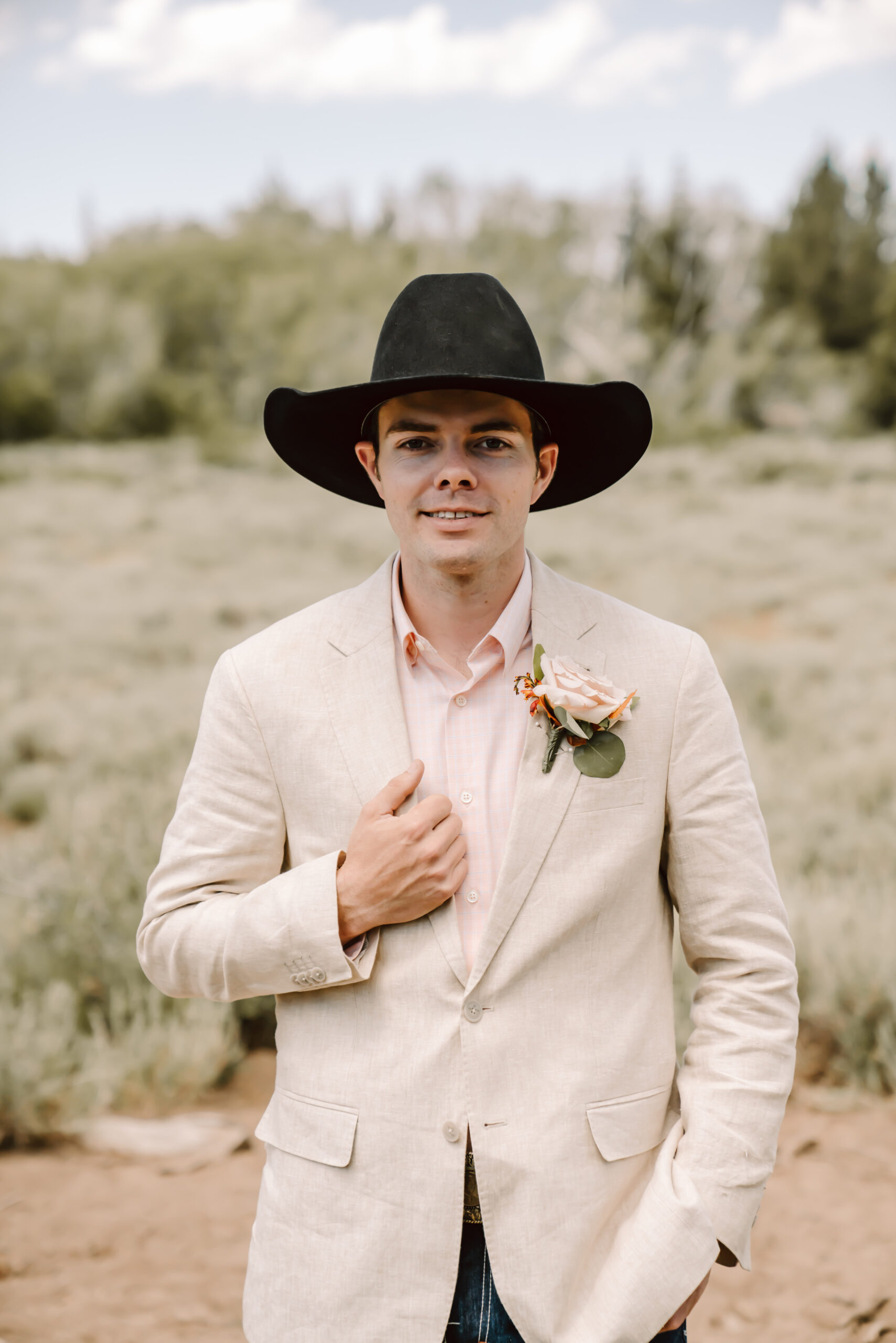 A groom wearing a white suit jacket and cowboy hat for his western themed elopement