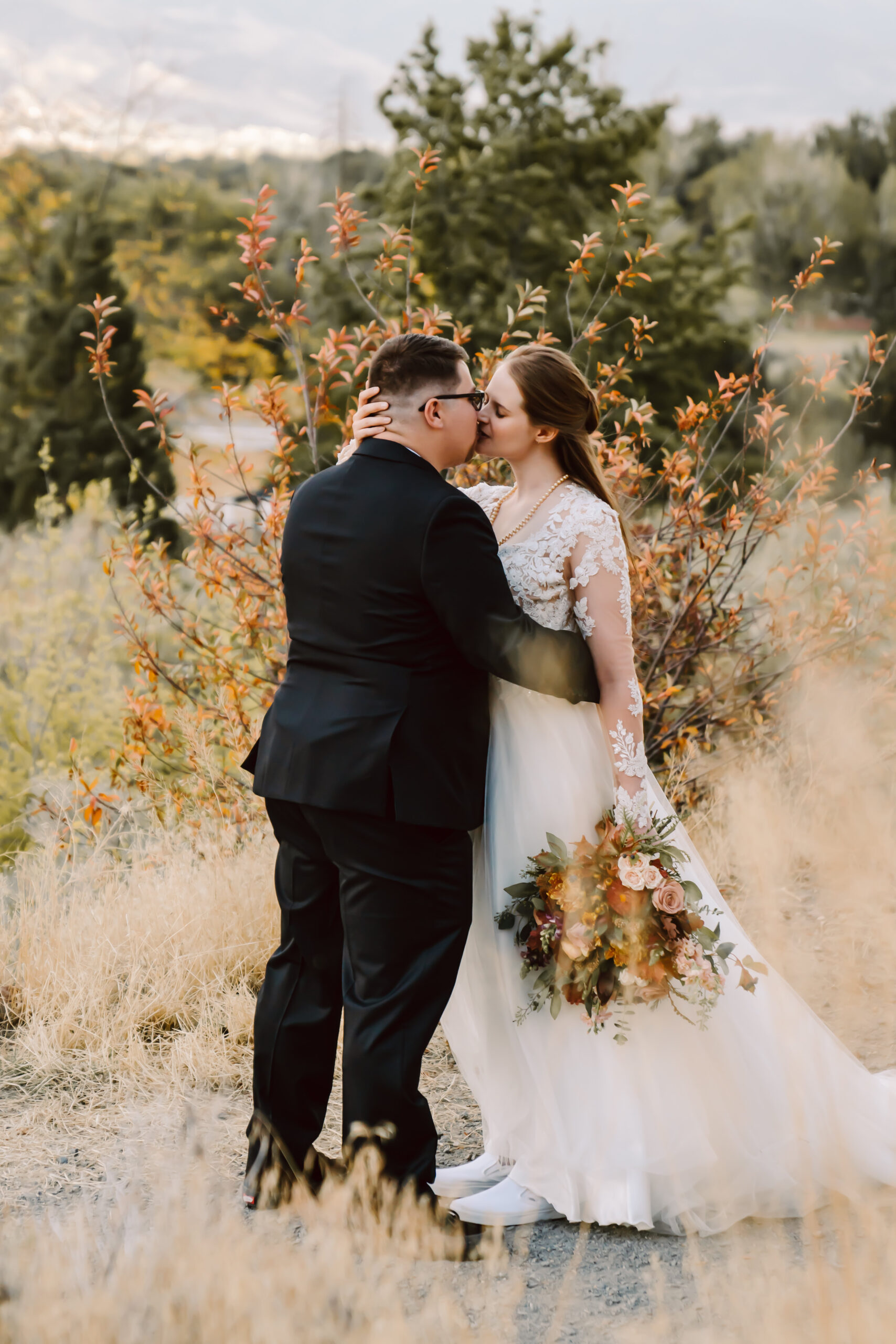 a bride and groom kissing in front of some fall colored leaves for their wedding day