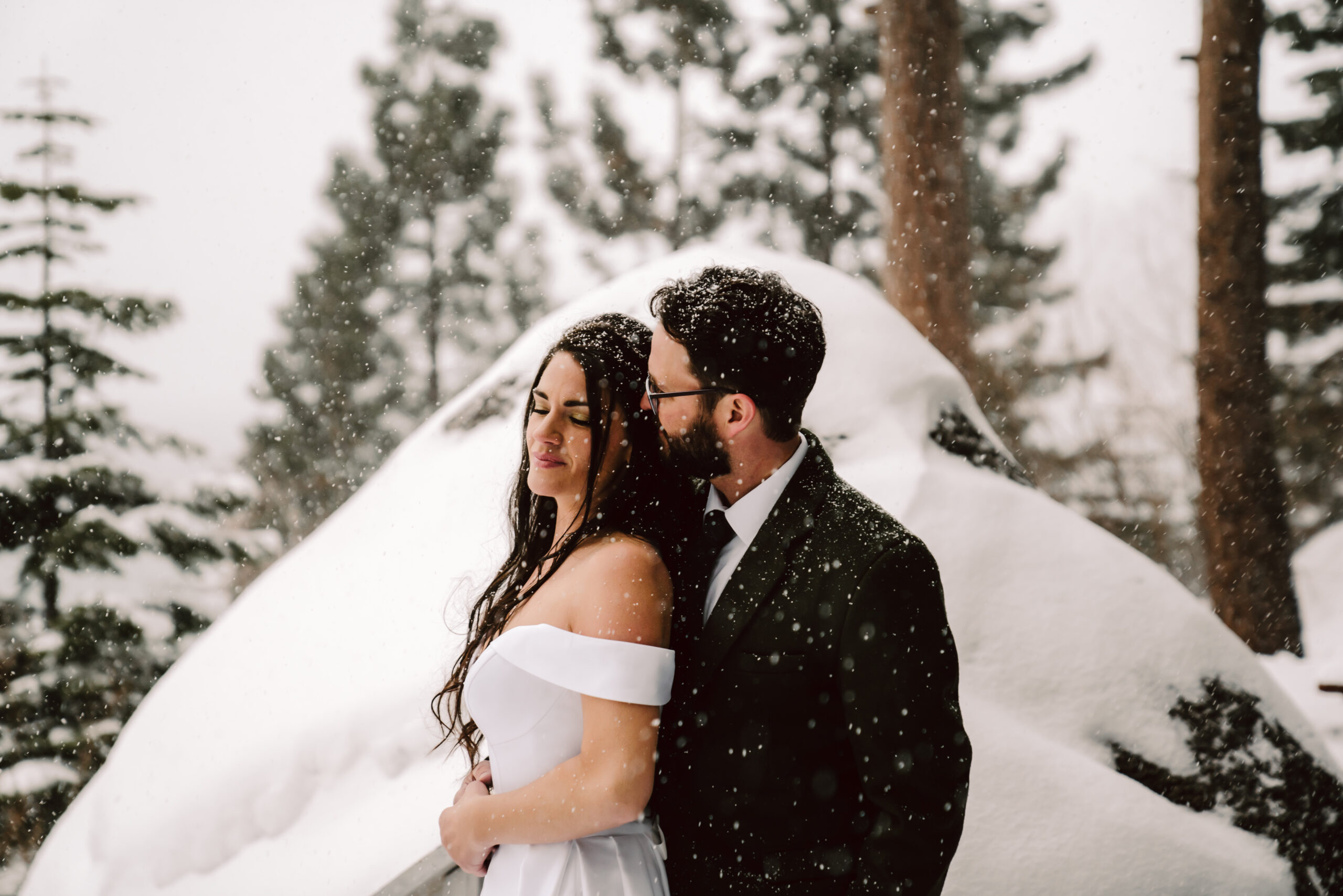 A groom holding his bride from behind and snow falling on their faces for a Winter wedding in Tahoe