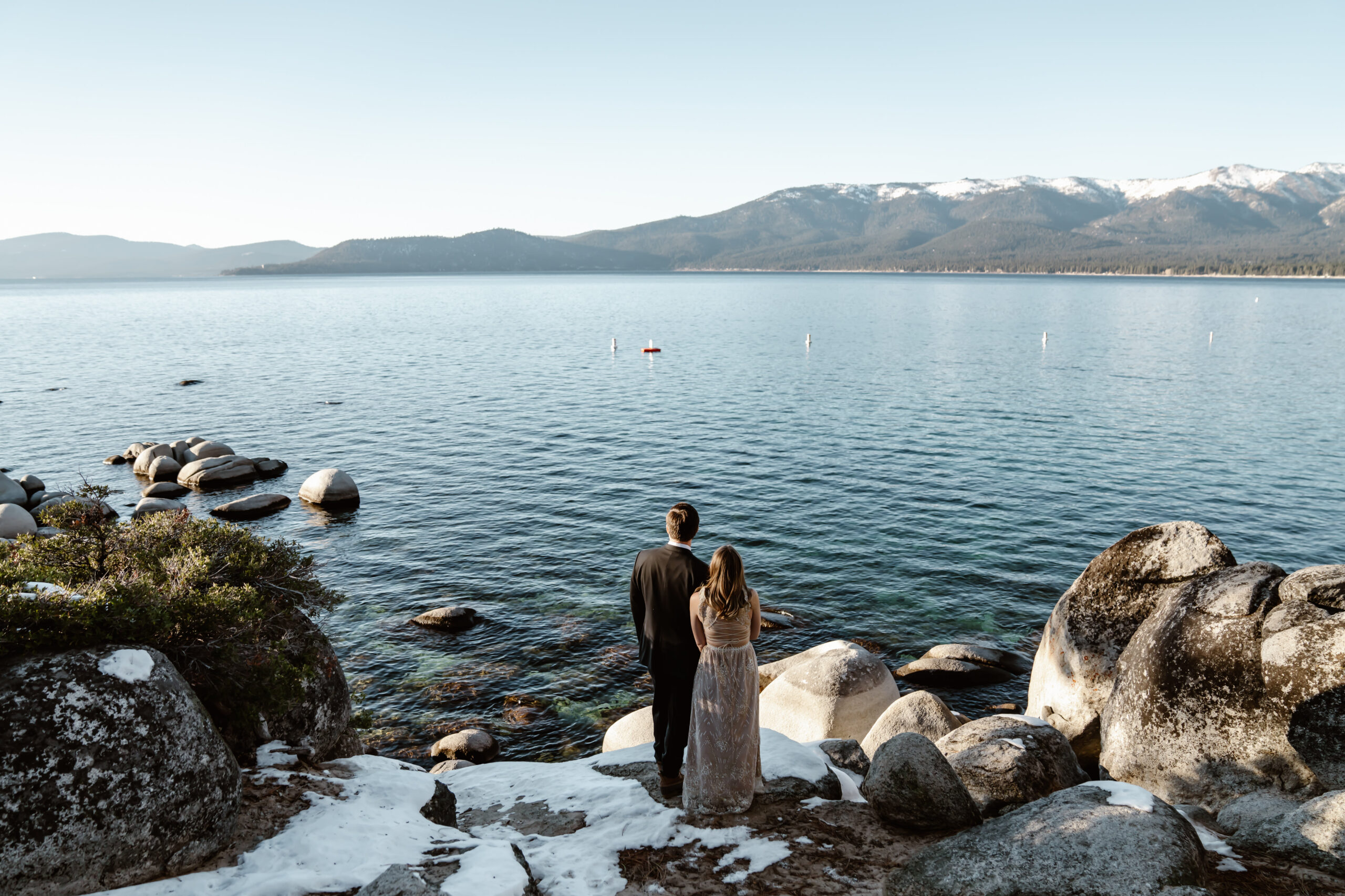 A bride and groom looking out onto Lake Tahoe standing in snowy rocks for their elopement day