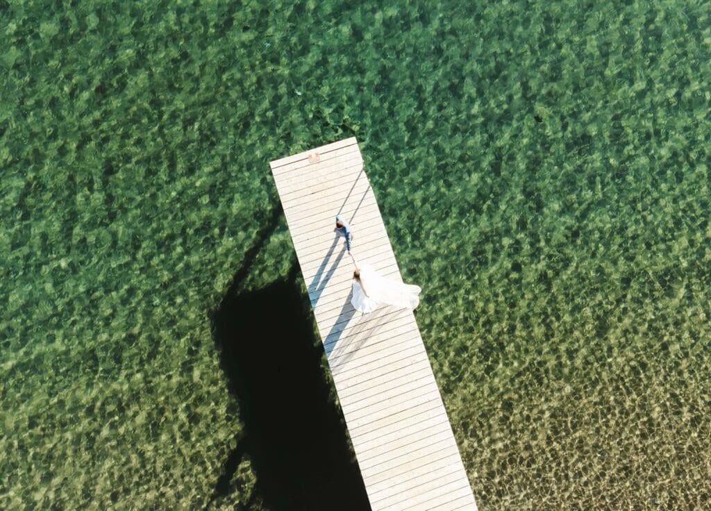 Aerial view of a Lake Tahoe elopement couple standing on a wooden dock surrounded by clear green-blue water