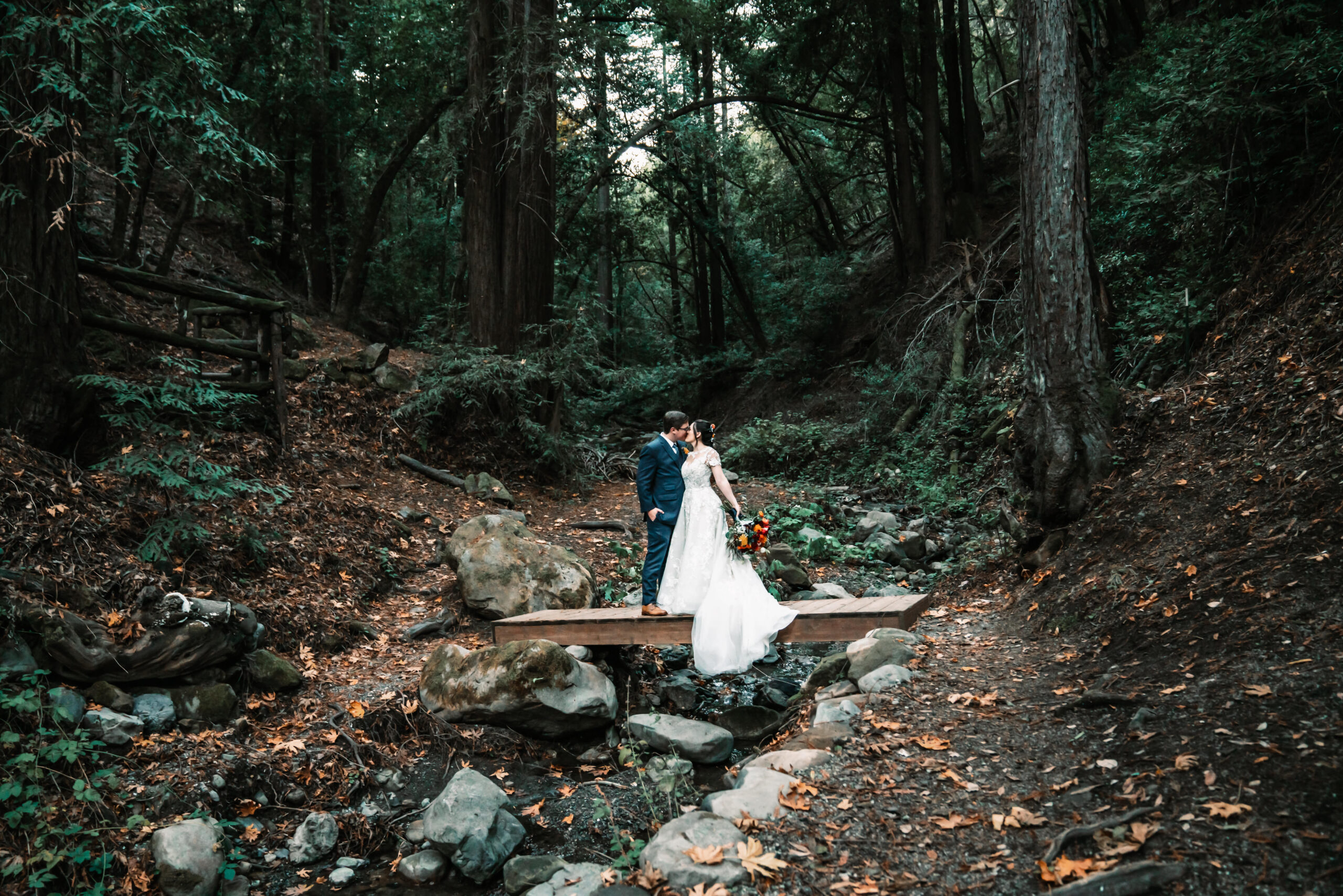 A bride and groom kissing and standing on a bridge in the forest for their wedding day