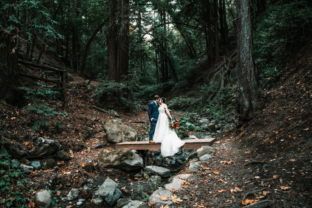 a wedding couple standing on a small bridge in the middle of the forest for the wedding day