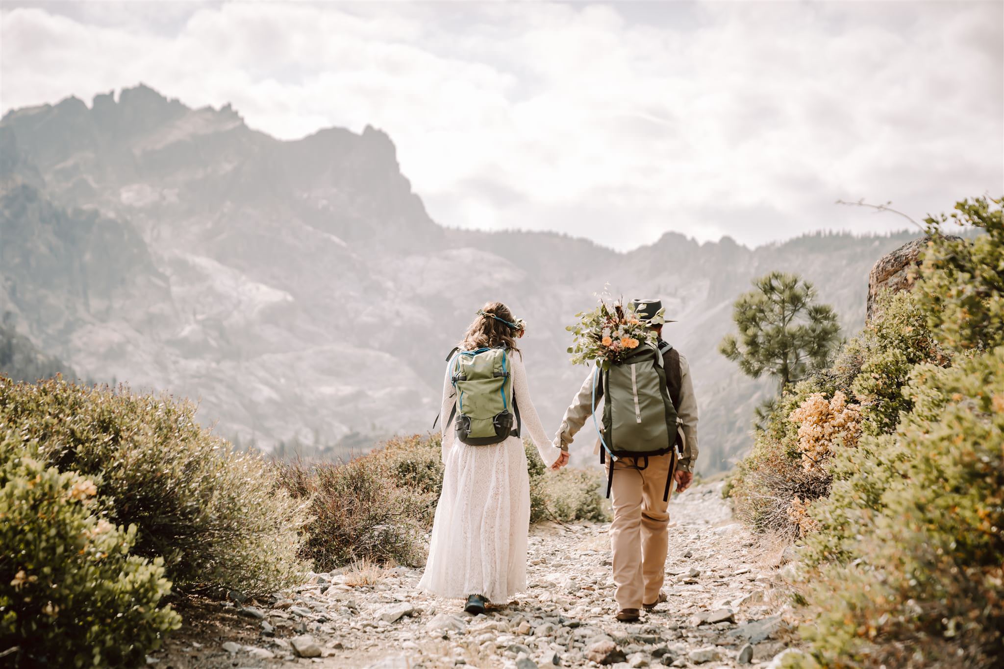 An elopement couple hiking a trail in their wedding attire with hiking backpack on
