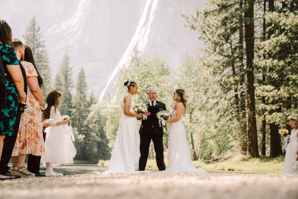 two brides having a wedding ceremony at Cathedral Beach in Yosemite National Park surrounded by friends and family and with mountain backdrops