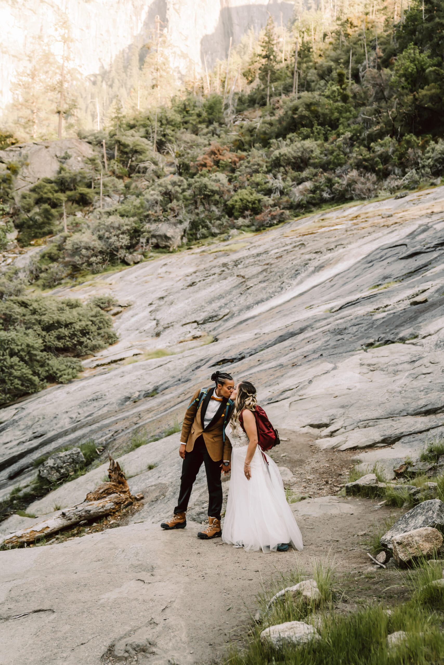 Two brides kissing with their hiking gear on overlooking the mountains in Yosemite