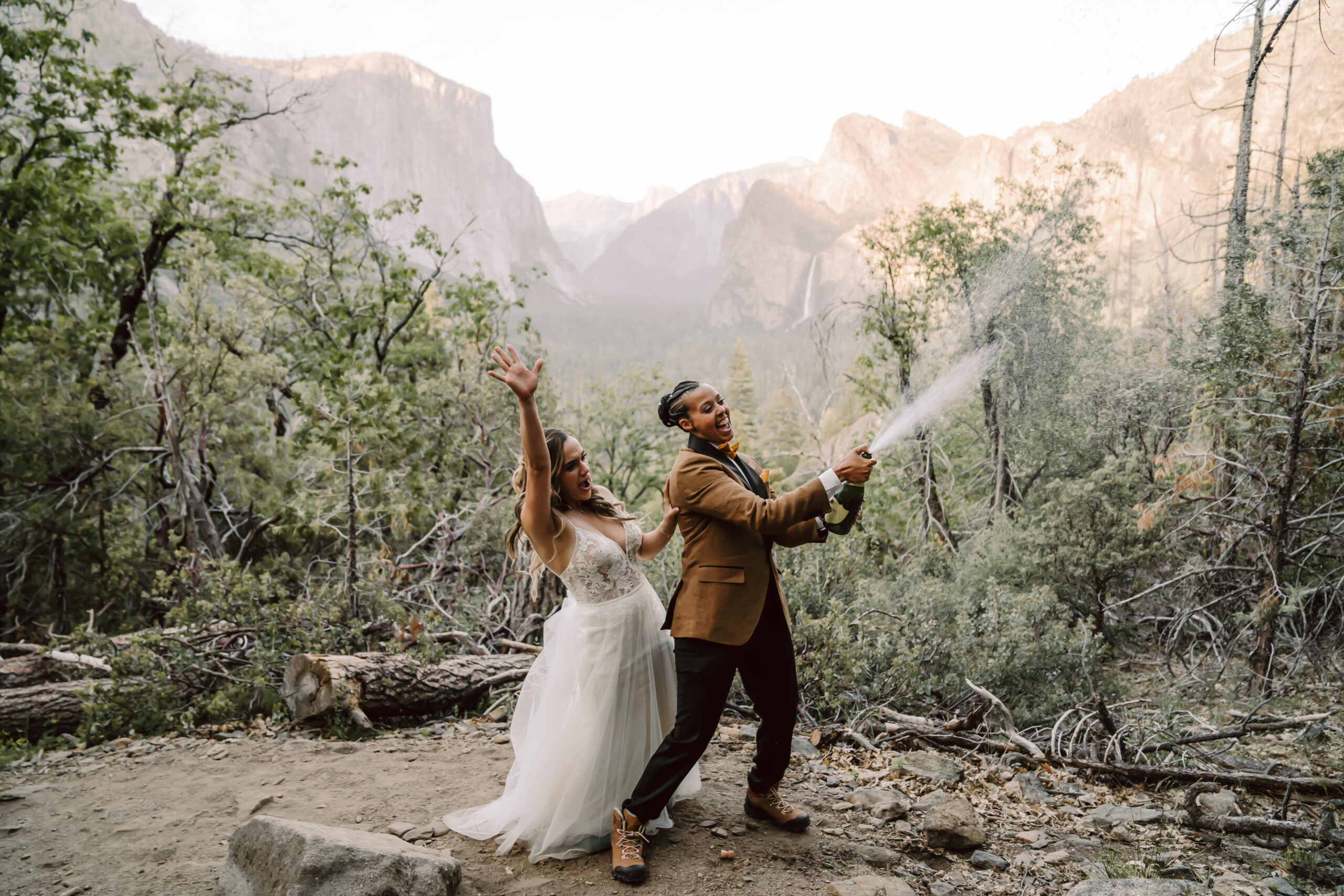 two brides spraying a champagne bottle at sunset overlooking Tunnel view for their elopement day in Yosemite
