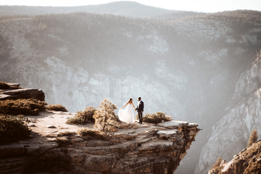 A elopement couple standing on the mountain cliff overlooking Yosemite valley on their elopement day