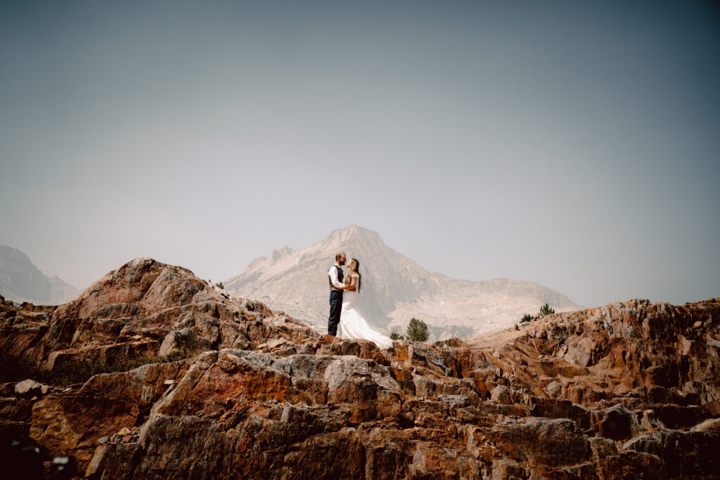 A wedding couple standing on red rocks kissing with a mountain as their backdrop for their adventure elopement