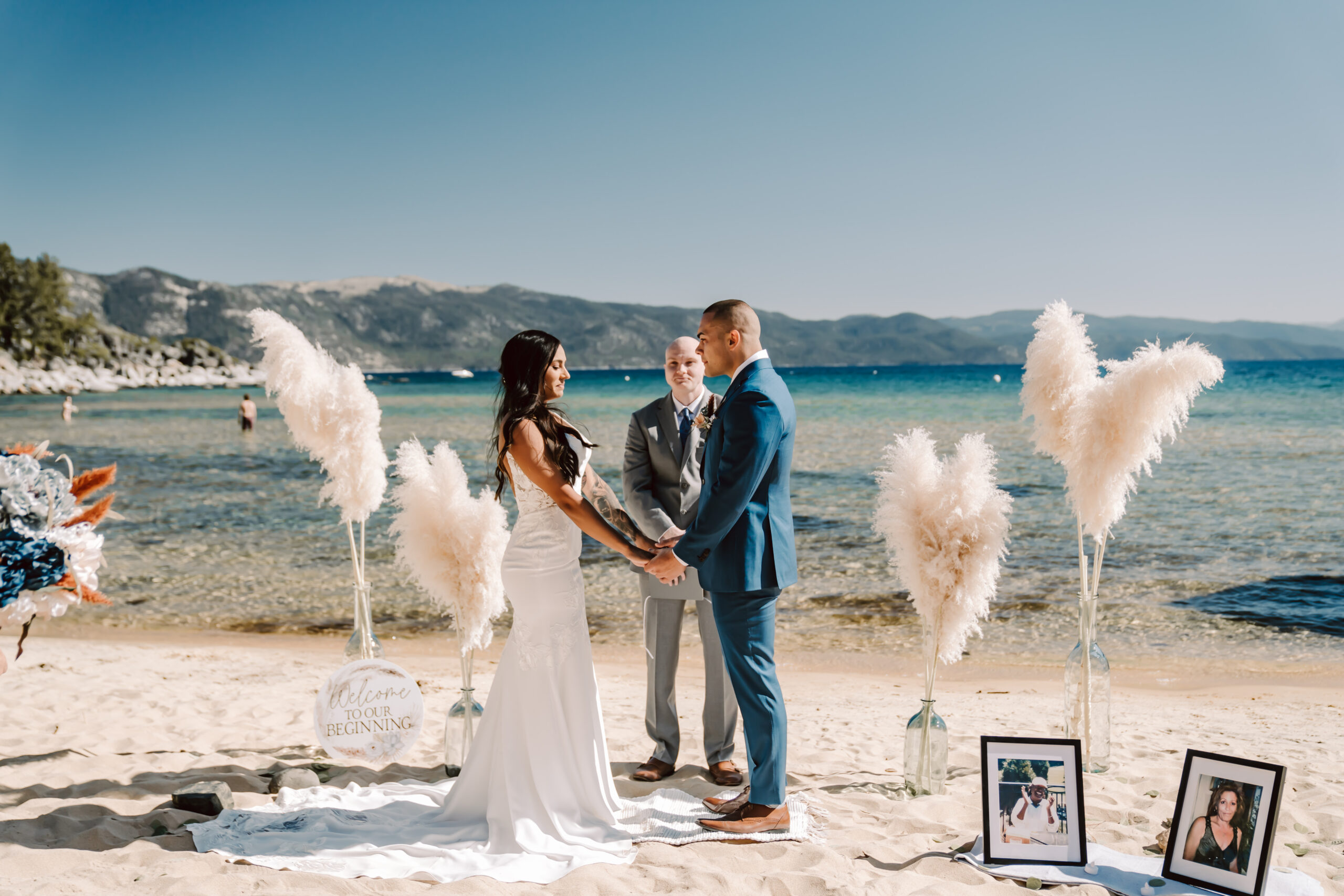 A bride and groom having a wedding ceremony on the beach in Lake Tahoe with beautiful feather decorations and mountains as the backdrop