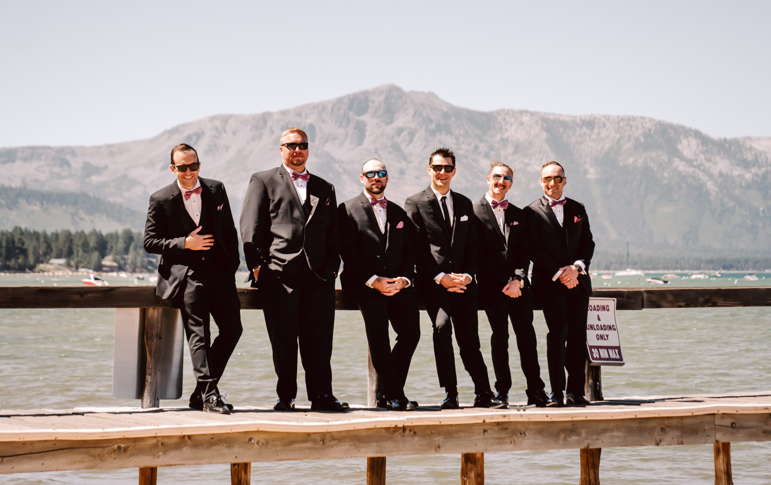 Groomsmen sitting on a dock on Lake Tahoe in their wedding tux and the mountains in the backdrop