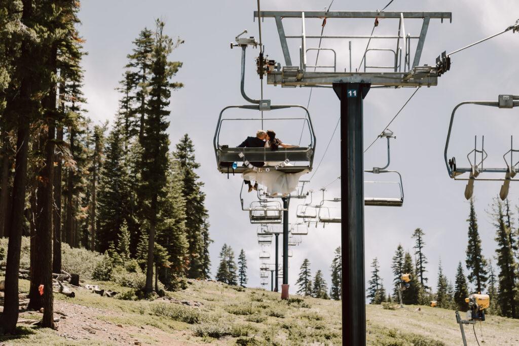 A bride and groom riding a ski chair lift with a sign on the back that says we eloped!